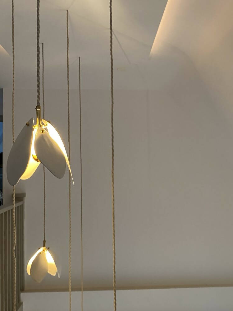 A close-up image of a white magnolia flower pendant light with a brass fitting and a gold-topped SES lamp,  available  to buy on the-salon.com. SALON curates the finest , unique, handmade pieces from the interior industry's best makers and brands. Shop luxury furniture, lighting, rugs, art, antiques and vintage pieces and accessories from SALON interior designed rooms.