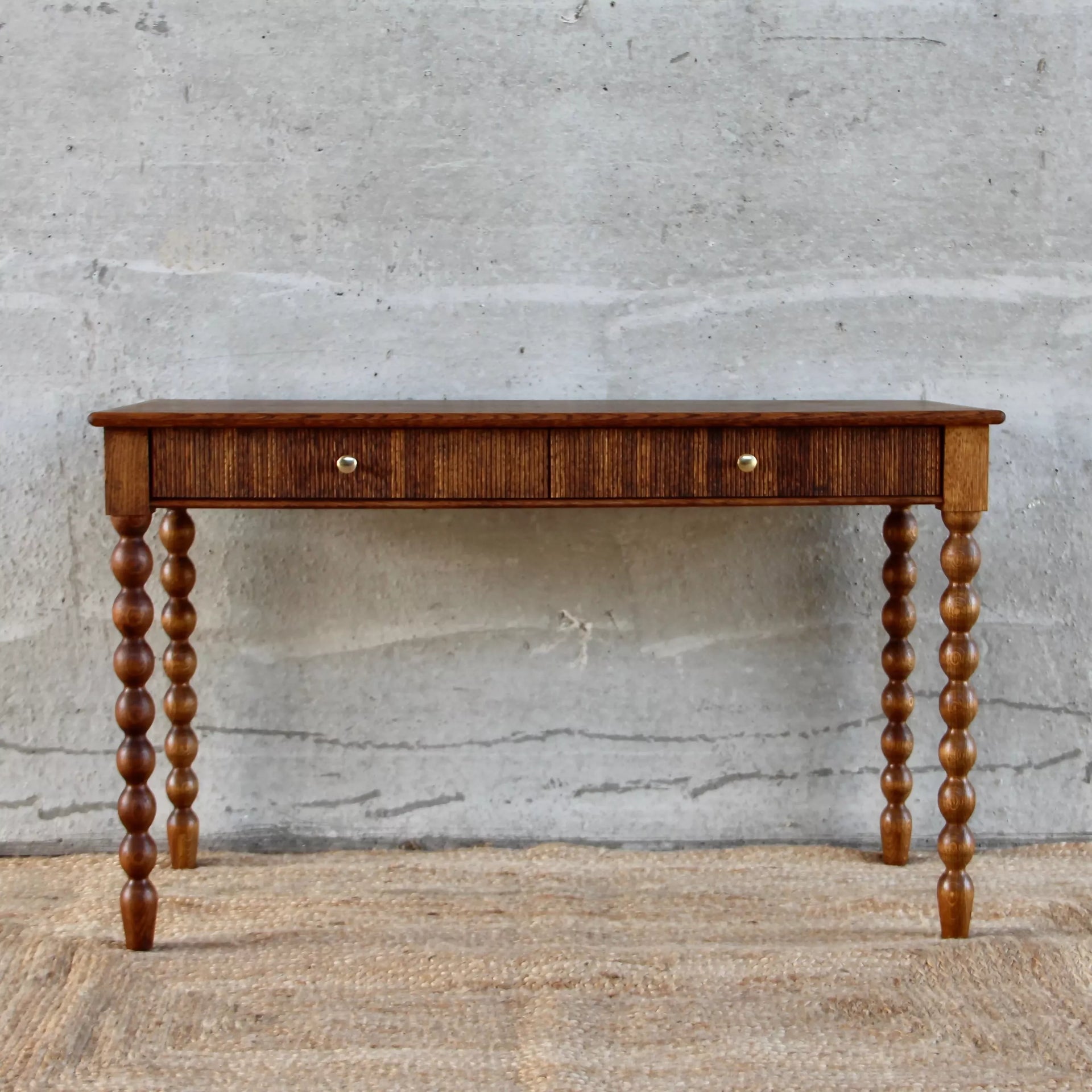 Wooden console table with spool legs against a gray concrete wall,available to buy from the-salon.com. SALON curates the finest unique handmade pieces from the interior industry's best makers and brands. Shop luxury furniture, lighting, rugs, art, antiques and vintage pieces and accessories from SALON interior designed rooms. 