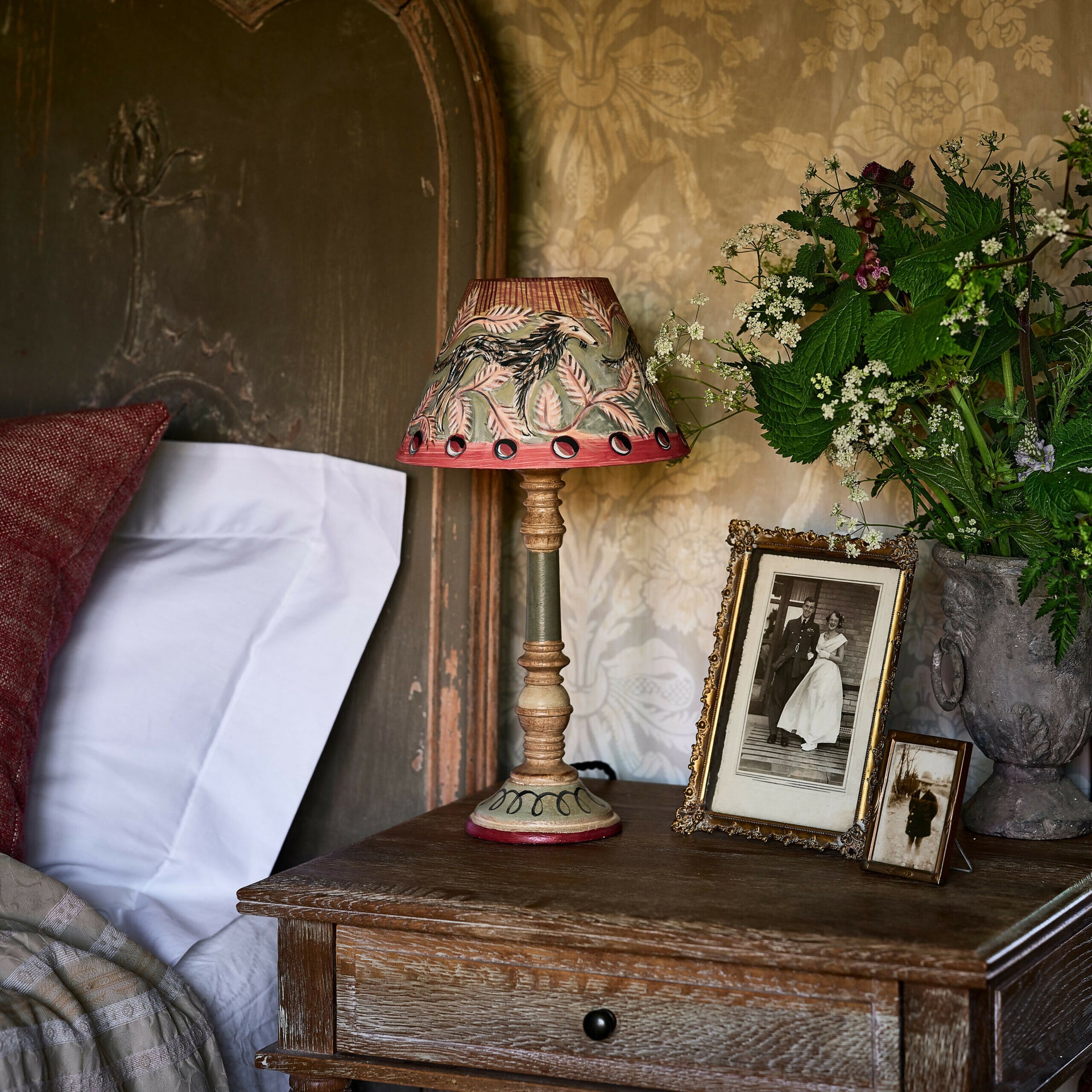 Vintage-style lamp on a wooden nightstand with decorative items and floral arrangement,  available  to buy on the-salon.com. SALON curates the finest , unique, handmade pieces from the interior industry's best makers and brands. Shop luxury furniture, lighting, rugs, art, antiques and vintage pieces and accessories from SALON interior designed rooms.