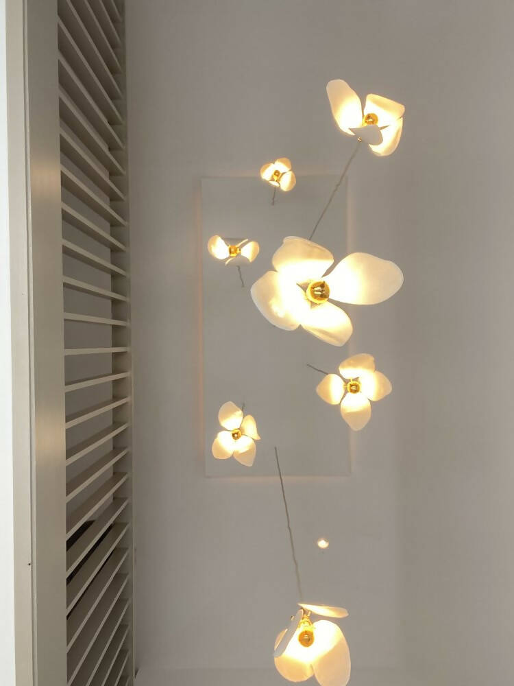 A close-up image of a white magnolia flower pendant light with a brass fitting and a gold-topped SES lamp,  available  to buy on the-salon.com. SALON curates the finest , unique, handmade pieces from the interior industry's best makers and brands. Shop luxury furniture, lighting, rugs, art, antiques and vintage pieces and accessories from SALON interior designed rooms.
