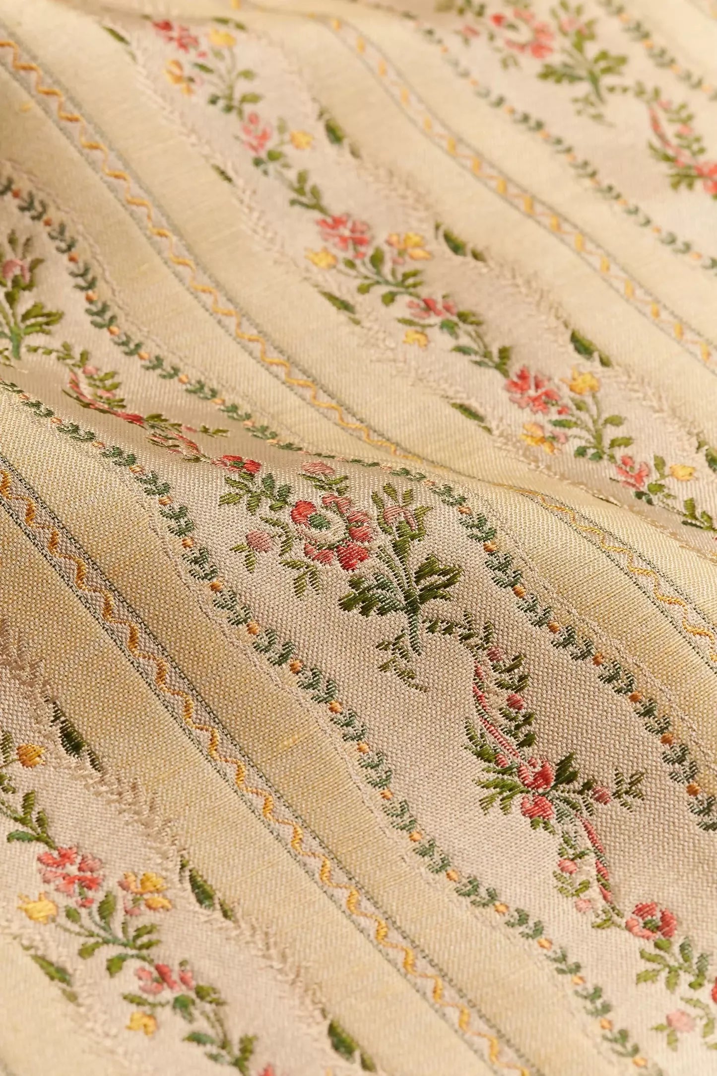 Close-up of Spitalfields stripe straw fabric with a jacquard weave, featuring floral motifs and silk leaves, in a warm honey tone,  available  to buy on the-salon.com. SALON curates the finest , unique, handmade pieces from the interior industry's best makers and brands. Shop luxury furniture, lighting, rugs, art, antiques and vintage pieces and accessories from SALON interior designed rooms.