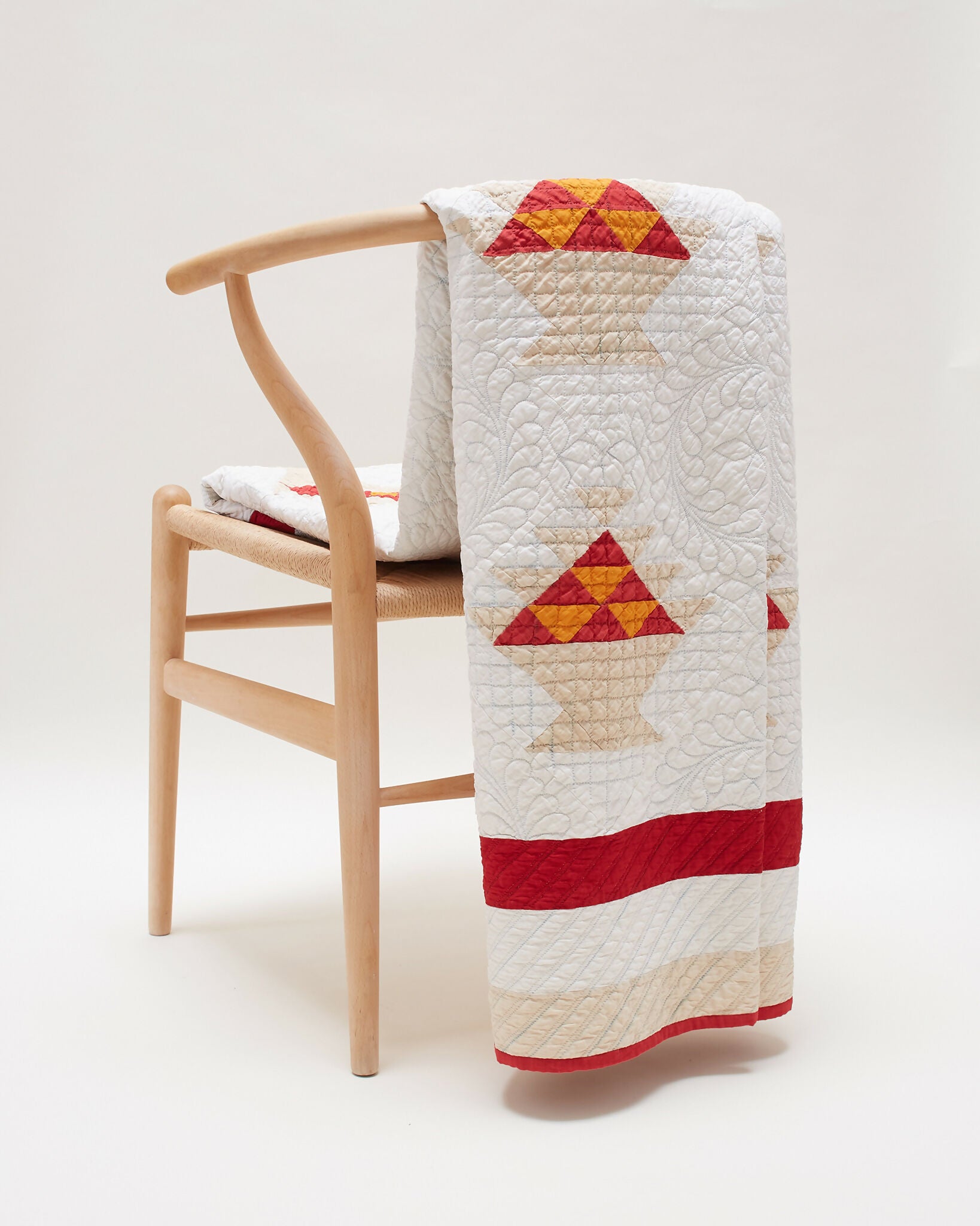 An antique patchwork quilt with a 'basket' pattern design, featuring red, orange, sand, and white colors, displayed draped over a wooden chair with a white background  available  to buy on the-salon.com. SALON curates the finest , unique, handmade pieces from the interior industry's best makers and brands. Shop luxury furniture, lighting, rugs, art, antiques and vintage pieces and accessories from SALON interior designed rooms.