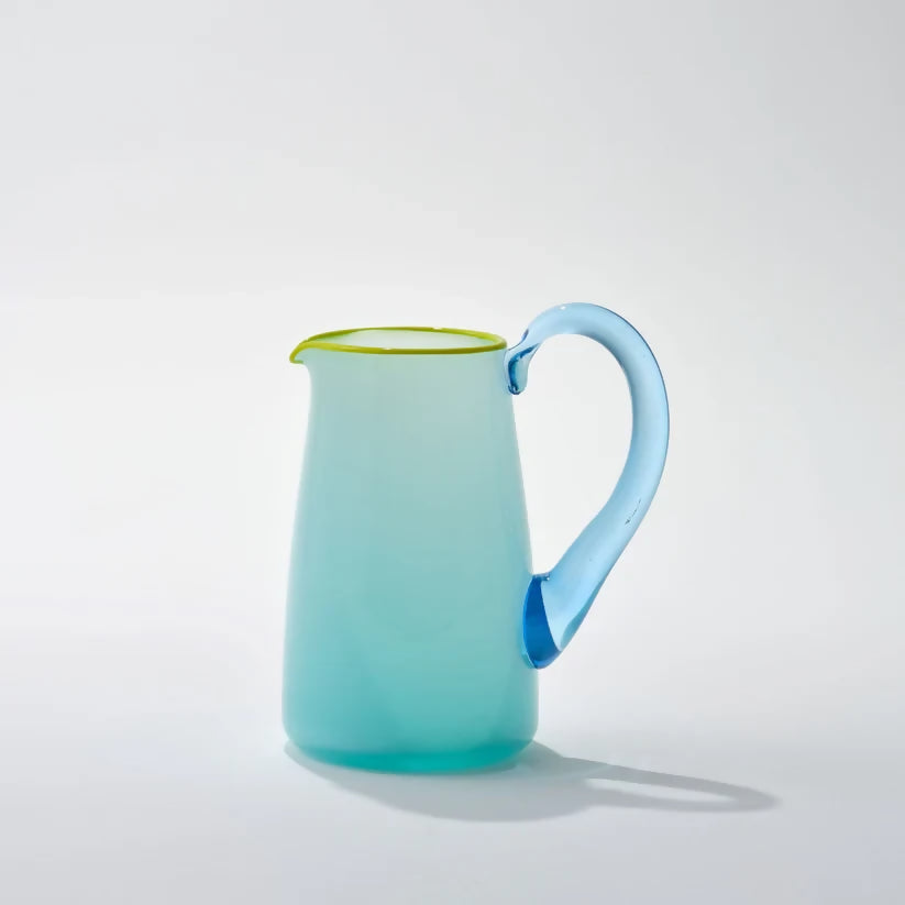 A hand-blown blue glass milk jug with an aqua blue handle and a celadon lip on a white background,  available  to buy on the-salon.com. SALON curates the finest , unique, handmade pieces from the interior industry's best makers and brands. Shop luxury furniture, lighting, rugs, art, antiques and vintage pieces and accessories from SALON interior designed rooms.