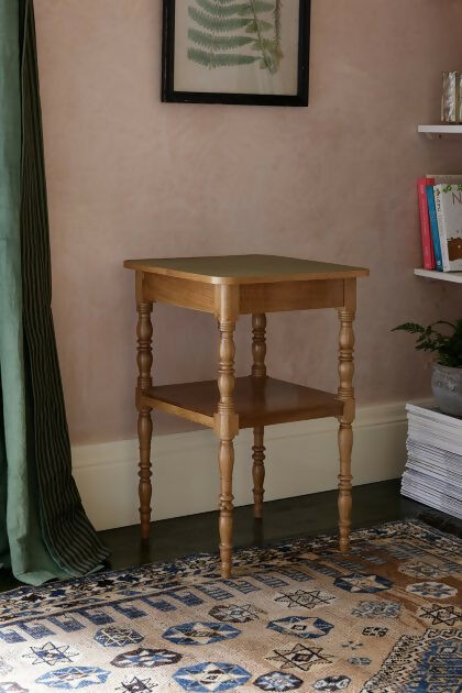 A brown wooden bedside table with a leather top, placed on a patterned carpet,  available  to buy on the-salon.com. SALON curates the finest , unique, handmade pieces from the interior industry's best makers and brands. Shop luxury furniture, lighting, rugs, art, antiques and vintage pieces and accessories from SALON interior designed rooms.