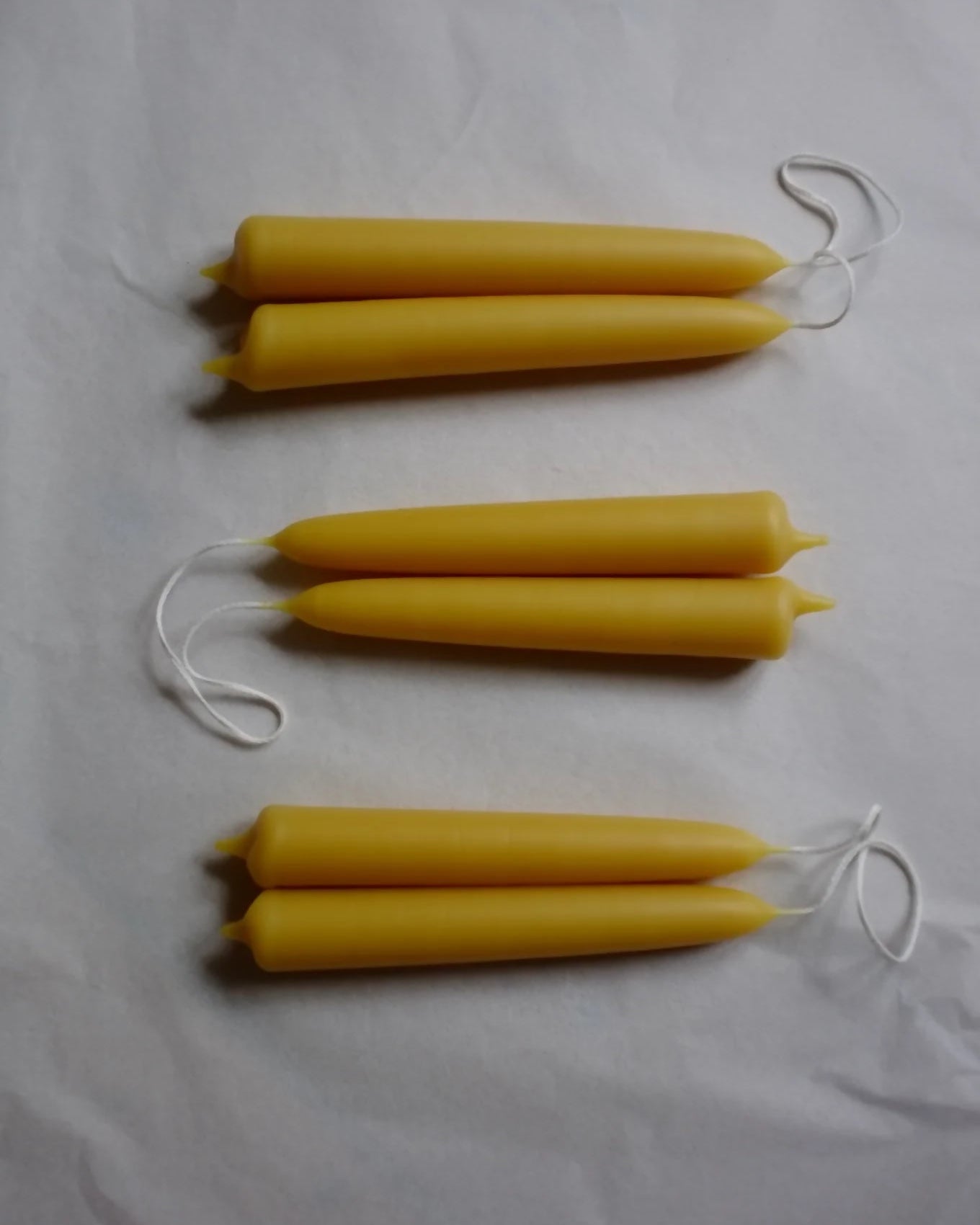 Three yellow candles with white strings on a white fabric background