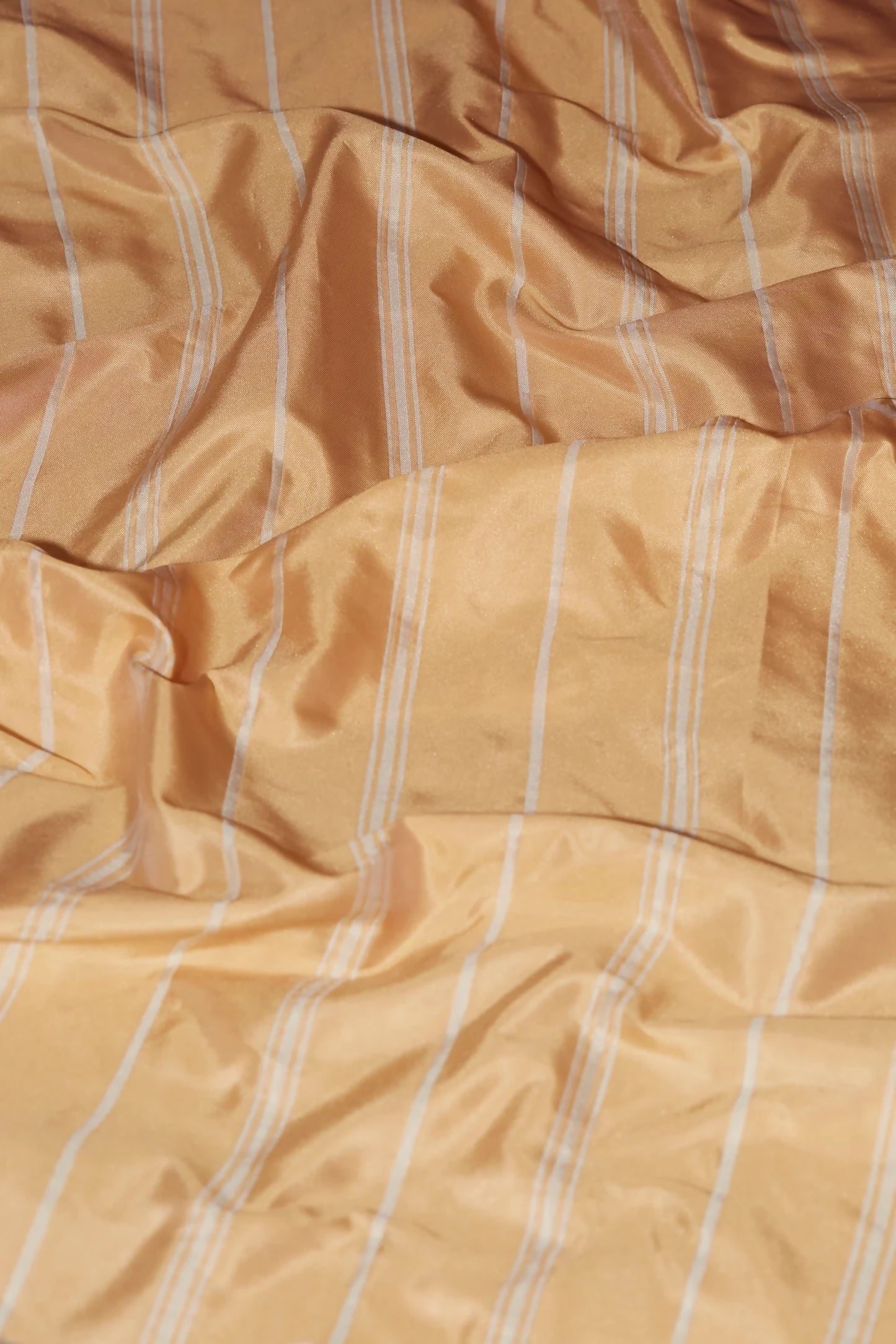 A crumpled piece of peach-colored taffeta fabric with white stripes, showcasing a smooth texture and reflective lustre,  available  to buy on the-salon.com. SALON curates the finest , unique, handmade pieces from the interior industry's best makers and brands. Shop luxury furniture, lighting, rugs, art, antiques and vintage pieces and accessories from SALON interior designed rooms.