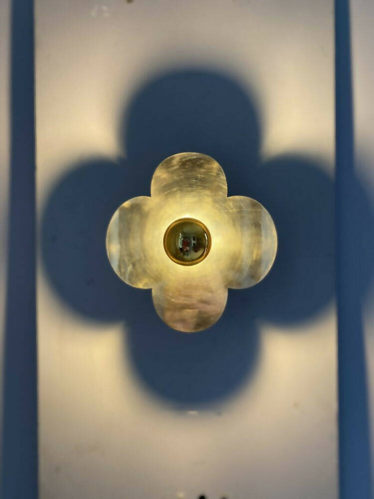 A wall light fixture with a gold-colored top and clear, possibly glass or acrylic, quatrefoil-shaped base,  available  to buy on the-salon.com. SALON curates the finest , unique, handmade pieces from the interior industry's best makers and brands. Shop luxury furniture, lighting, rugs, art, antiques and vintage pieces and accessories from SALON interior designed rooms.
