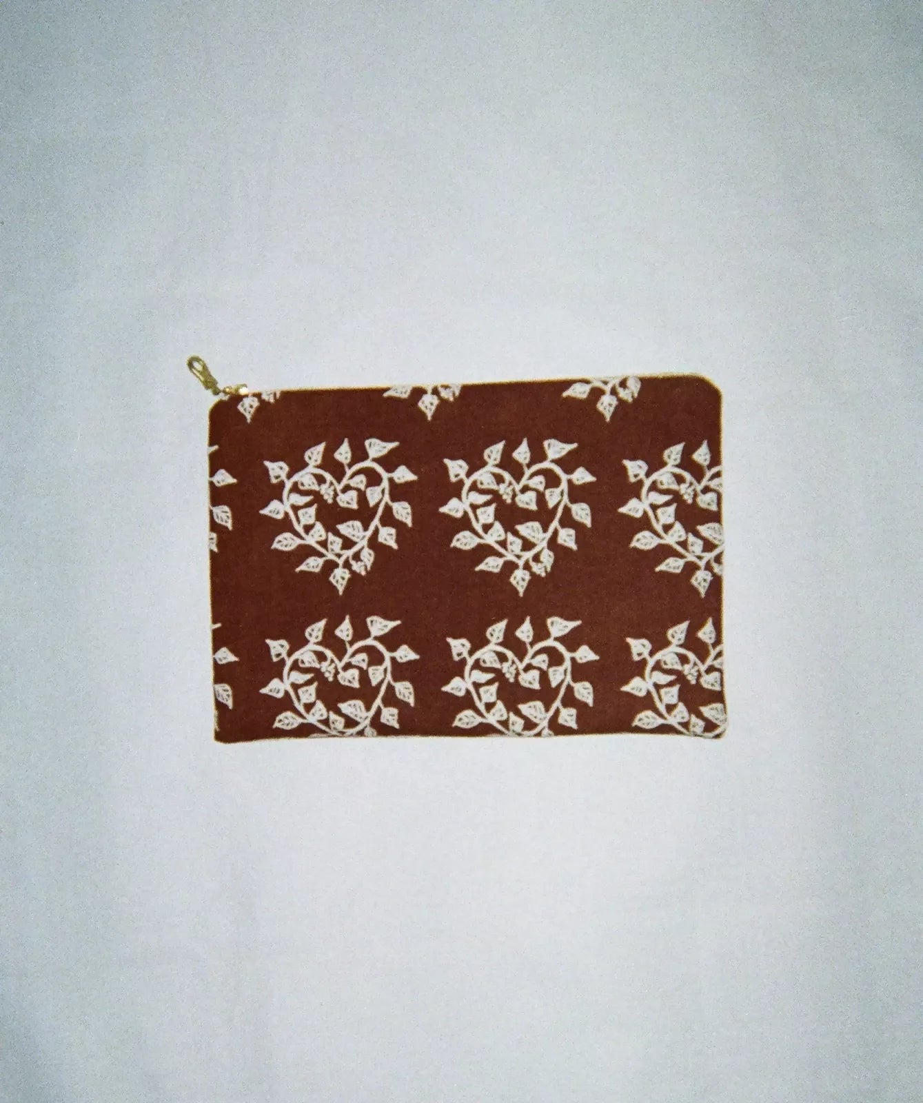 A brown cosmetic pouch with a screen printed pattern of hearts and leaves, lined with a green zipper,  available  to buy on the-salon.com. SALON curates the finest , unique, handmade pieces from the interior industry's best makers and brands. Shop luxury furniture, lighting, rugs, art, antiques and vintage pieces and accessories from SALON interior designed rooms.