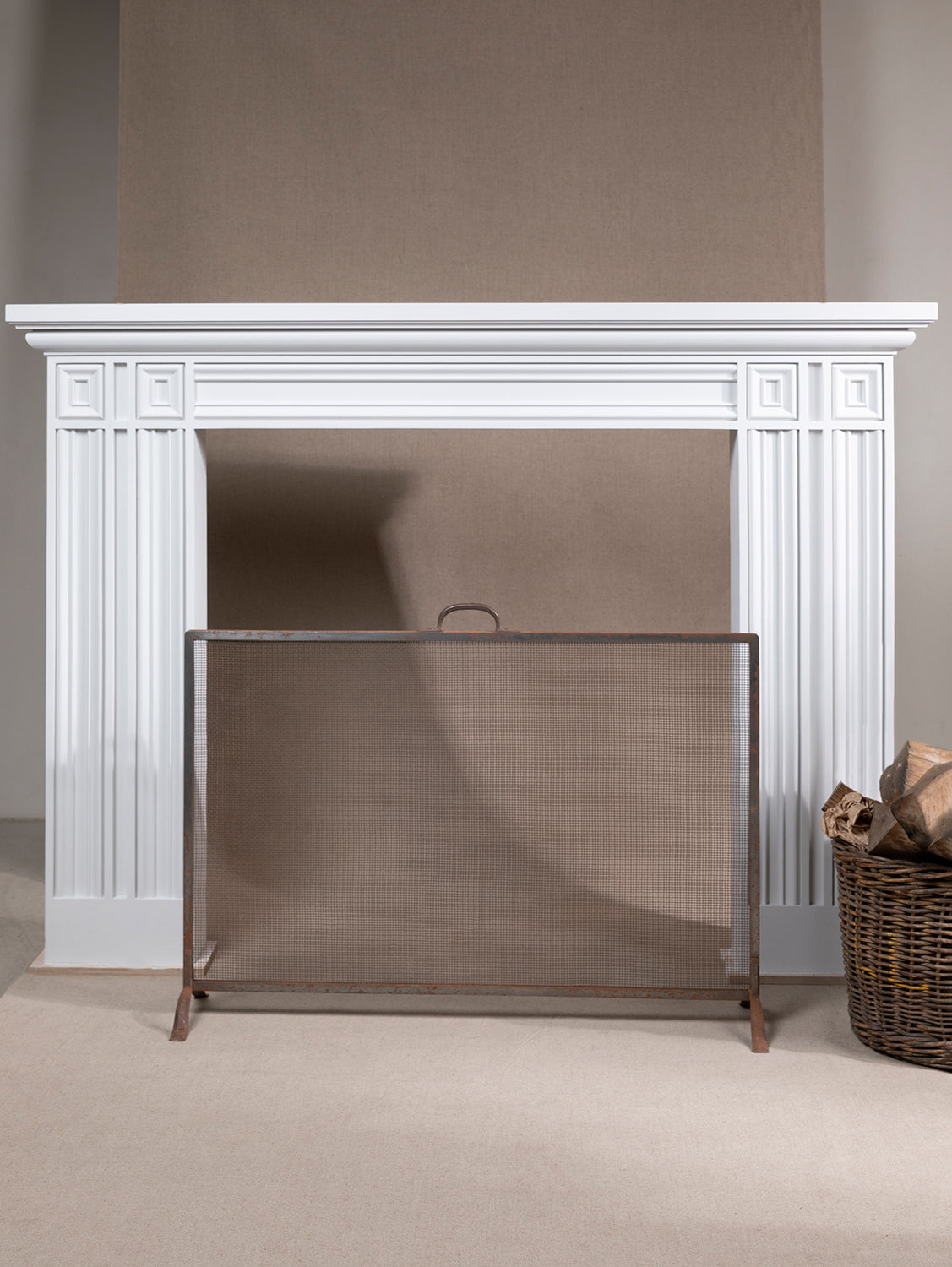 A white neo-classical style fireplace made of wood, with a visible metal screen in front,  available  to buy on the-salon.com. SALON curates the finest , unique, handmade pieces from the interior industry's best makers and brands. Shop luxury furniture, lighting, rugs, art, antiques and vintage pieces and accessories from SALON interior designed rooms.