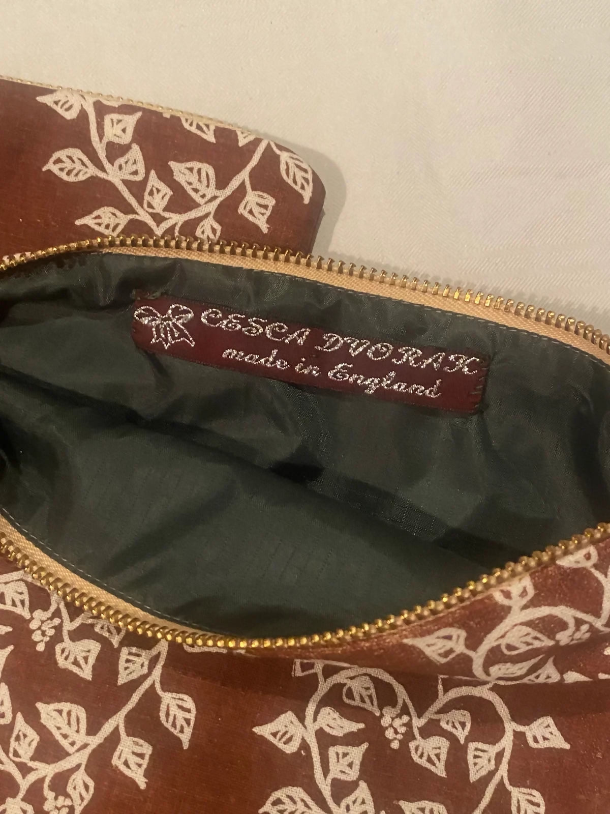 A brown cosmetic pouch with a screen printed pattern of hearts and leaves, lined with a green zipper,  available  to buy on the-salon.com. SALON curates the finest , unique, handmade pieces from the interior industry's best makers and brands. Shop luxury furniture, lighting, rugs, art, antiques and vintage pieces and accessories from SALON interior designed rooms.