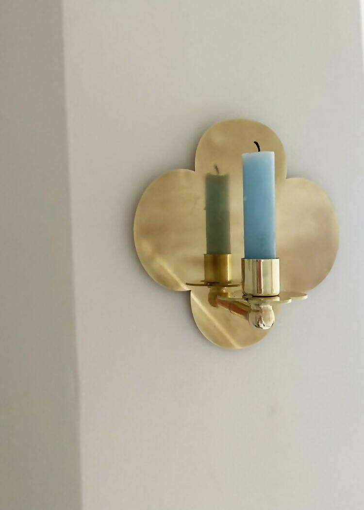 A solid brass wall-mounted candle sconce in the shape of a quatrefoil with a candle,  available  to buy on the-salon.com. SALON curates the finest , unique, handmade pieces from the interior industry's best makers and brands. Shop luxury furniture, lighting, rugs, art, antiques and vintage pieces and accessories from SALON interior designed rooms.