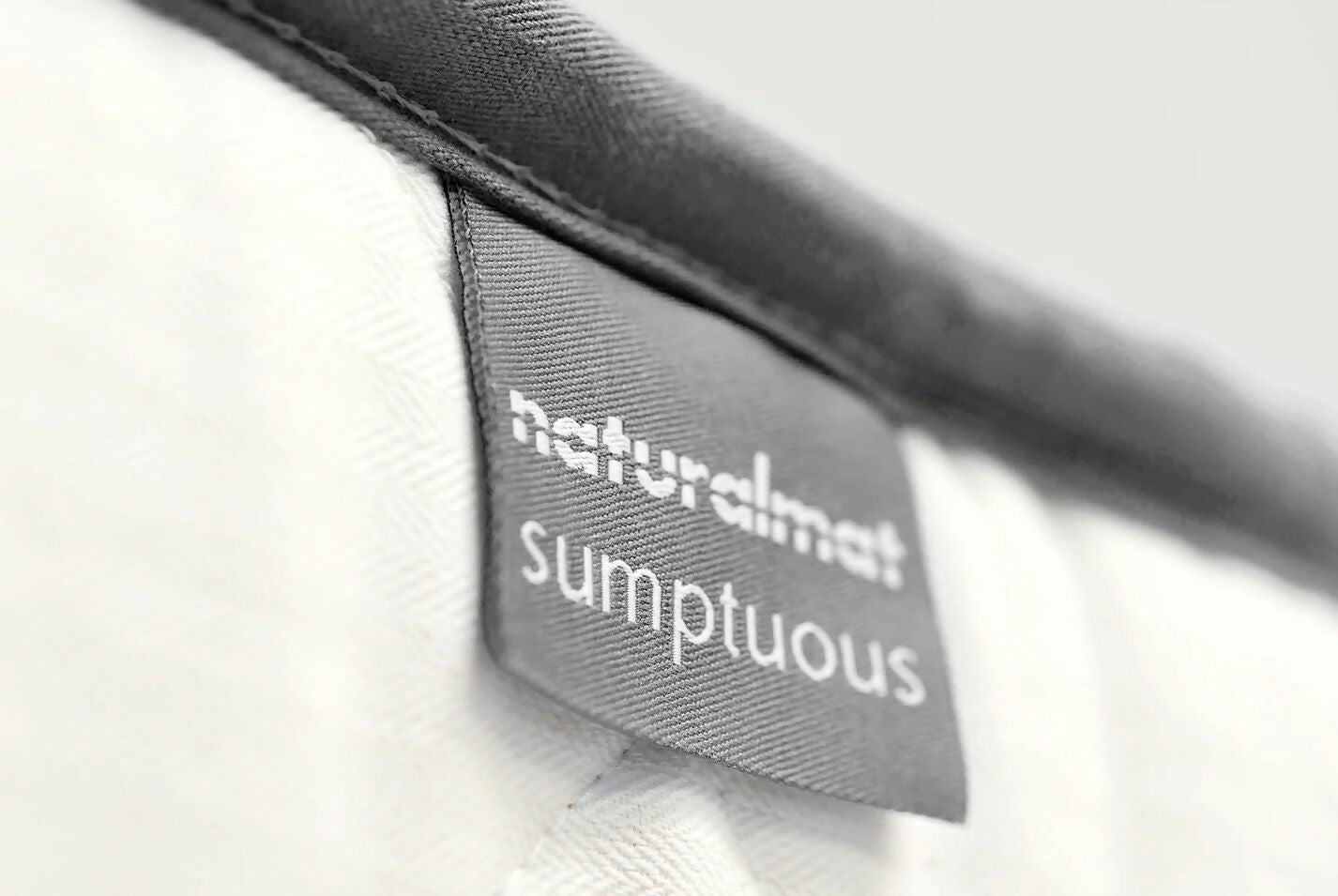 Close-up of a mattress tag with 'naturalmat sumptuous' branding on a white background,  available  to buy on the-salon.com. SALON curates the finest , unique, handmade pieces from the interior industry's best makers and brands. Shop luxury furniture, lighting, rugs, art, antiques and vintage pieces and accessories from SALON interior designed rooms.