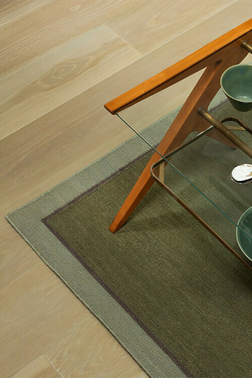Top view of a flatweave dhurrie rug in a plain green colour with a border,  available  to buy on the-salon.com. SALON curates the finest , unique, handmade pieces from the interior industry's best makers and brands. Shop luxury furniture, lighting, rugs, art, antiques and vintage pieces and accessories from SALON interior designed rooms.