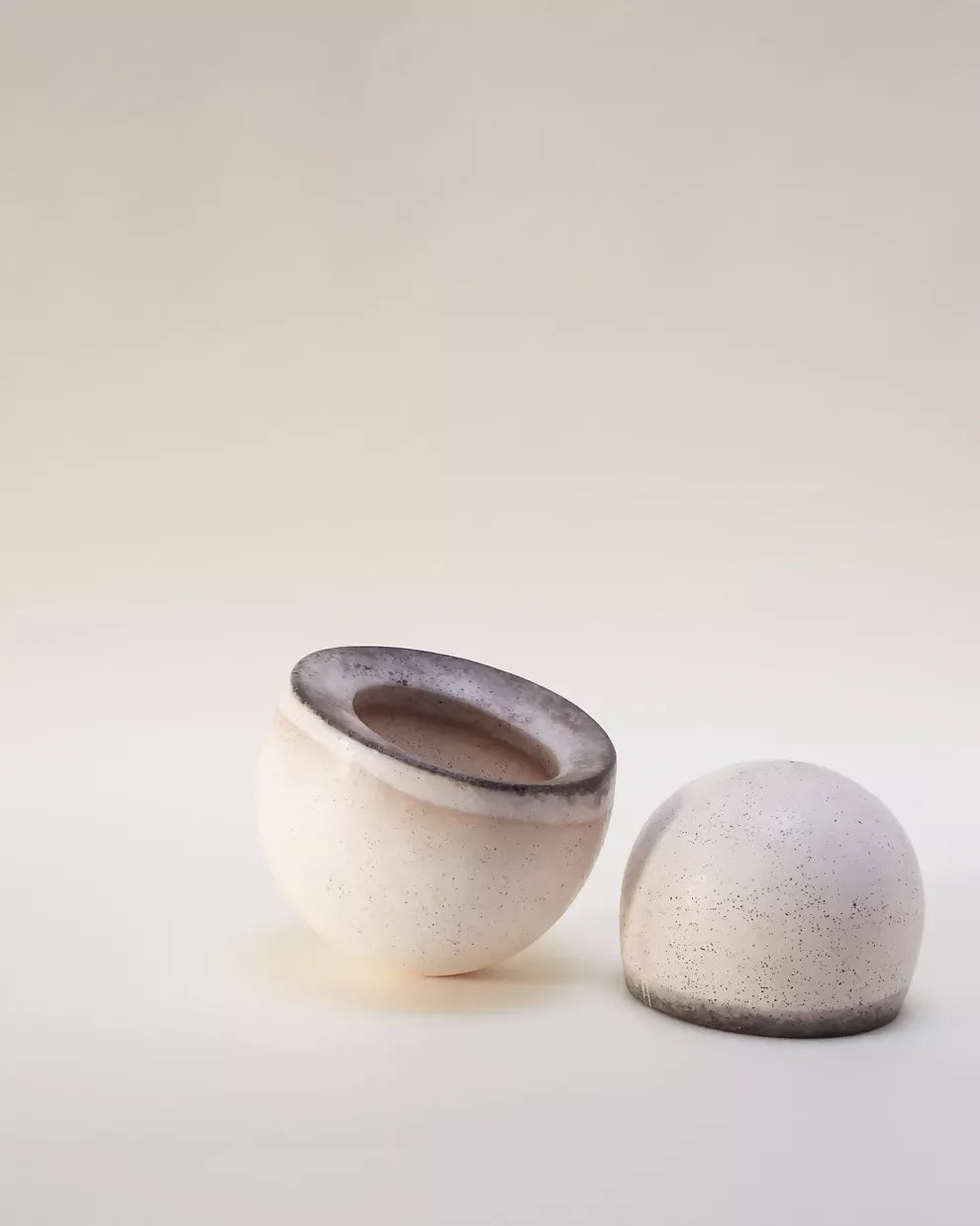 A pair of beige ceramic bowls with a textured surface, one with an open top view and the other upside down, showing the base of the bowl,  available  to buy on the-salon.com. SALON curates the finest , unique, handmade pieces from the interior industry's best makers and brands. Shop luxury furniture, lighting, rugs, art, antiques and vintage pieces and accessories from SALON interior designed rooms.