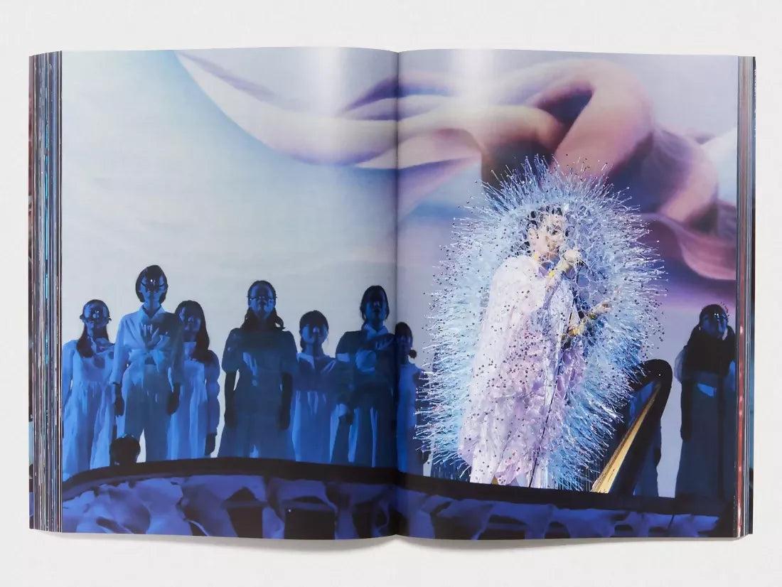 An Image of an open book, featuring whimsical colours, pastels for the background and a woman singing on stage in the foreground whilst other women without the spotlight, stand in the back, available  to buy on the-salon.com. SALON curates the finest , unique, handmade pieces from the interior industry's best makers and brands. Shop luxury furniture, lighting, rugs, art, antiques and vintage pieces and accessories from SALON interior designed rooms.