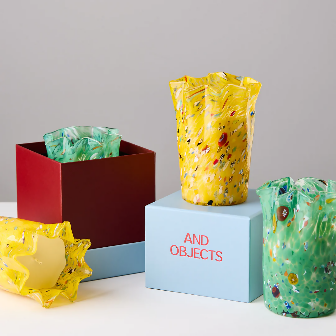 Two custom hand-blown glass candles, in green and yellow, embedded colourful glass pieces, displayed alongside its lid, on a white surface,  available  to buy on the-salon.com. SALON curates the finest , unique, handmade pieces from the interior industry's best makers and brands. Shop luxury furniture, lighting, rugs, art, antiques and vintage pieces and accessories from SALON interior designed rooms.