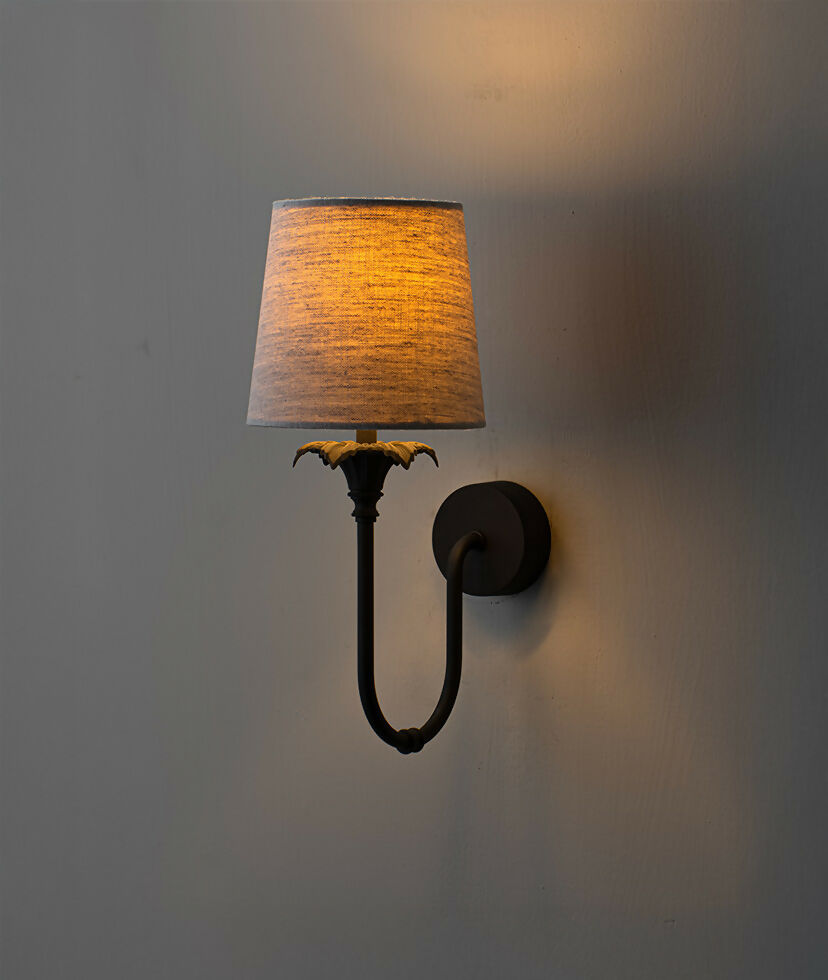 A wall-mounted light fixture with a black-colored metal arm and a white, solid-patterned lampshade,  available  to buy on the-salon.com. SALON curates the finest , unique, handmade pieces from the interior industry's best makers and brands. Shop luxury furniture, lighting, rugs, art, antiques and vintage pieces and accessories from SALON interior designed rooms.