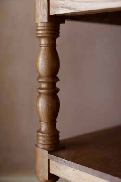A close up on the wooden legs on the  brown wooden bedside table with a leather top, placed on a patterned carpet,  available  to buy on the-salon.com. SALON curates the finest , unique, handmade pieces from the interior industry's best makers and brands. Shop luxury furniture, lighting, rugs, art, antiques and vintage pieces and accessories from SALON interior designed rooms.