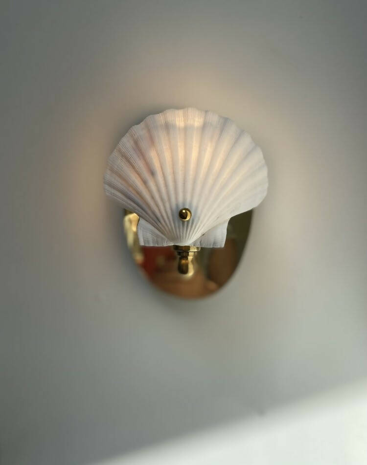 A wall light fixture with a chalky white scallop shell finish mounted on a polished brass backplate,  available  to buy on the-salon.com. SALON curates the finest , unique, handmade pieces from the interior industry's best makers and brands. Shop luxury furniture, lighting, rugs, art, antiques and vintage pieces and accessories from SALON interior designed rooms.
