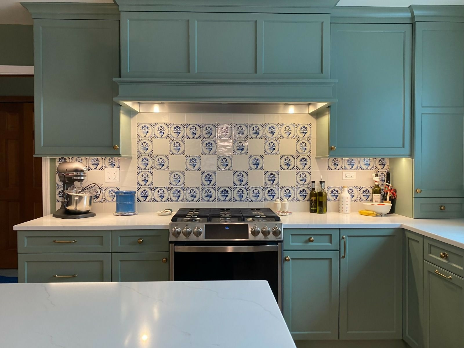 Kitchen with teal cabinets, white countertops, and a tiled backsplash,  available  to buy on the-salon.com. SALON curates the finest , unique, handmade pieces from the interior industry's best makers and brands. Shop luxury furniture, lighting, rugs, art, antiques and vintage pieces and accessories from SALON interior designed rooms.