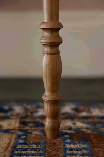 A close up on the wooden legs on the  brown wooden bedside table with a leather top, placed on a patterned carpet,  available  to buy on the-salon.com. SALON curates the finest , unique, handmade pieces from the interior industry's best makers and brands. Shop luxury furniture, lighting, rugs, art, antiques and vintage pieces and accessories from SALON interior designed rooms.