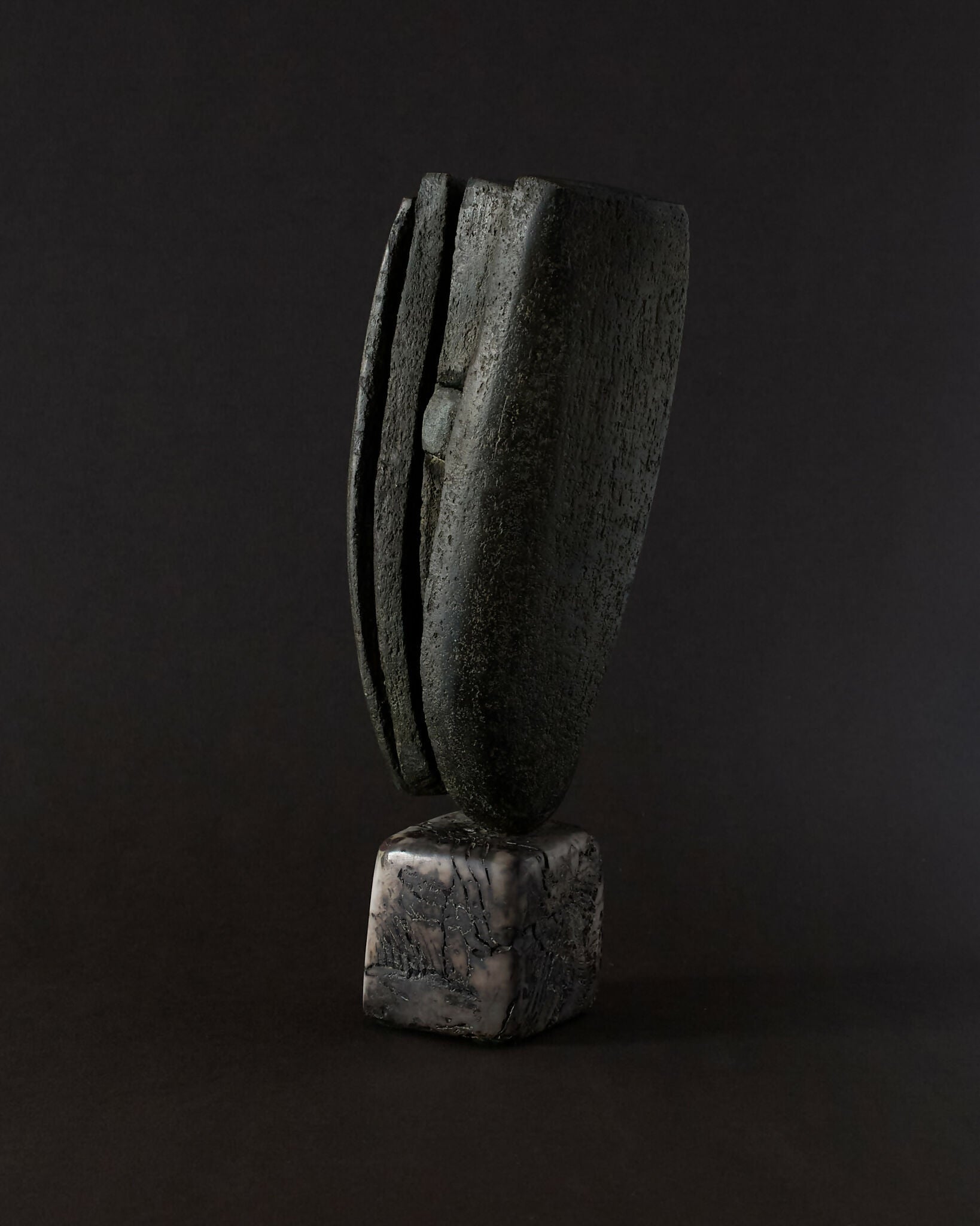 A tall, slate-grey, textured abstract stoneware sculpture with linear details, sitting on a polished ceramic base,  available  to buy on the-salon.com. SALON curates the finest , unique, handmade pieces from the interior industry's best makers and brands. Shop luxury furniture, lighting, rugs, art, antiques and vintage pieces and accessories from SALON interior designed rooms.