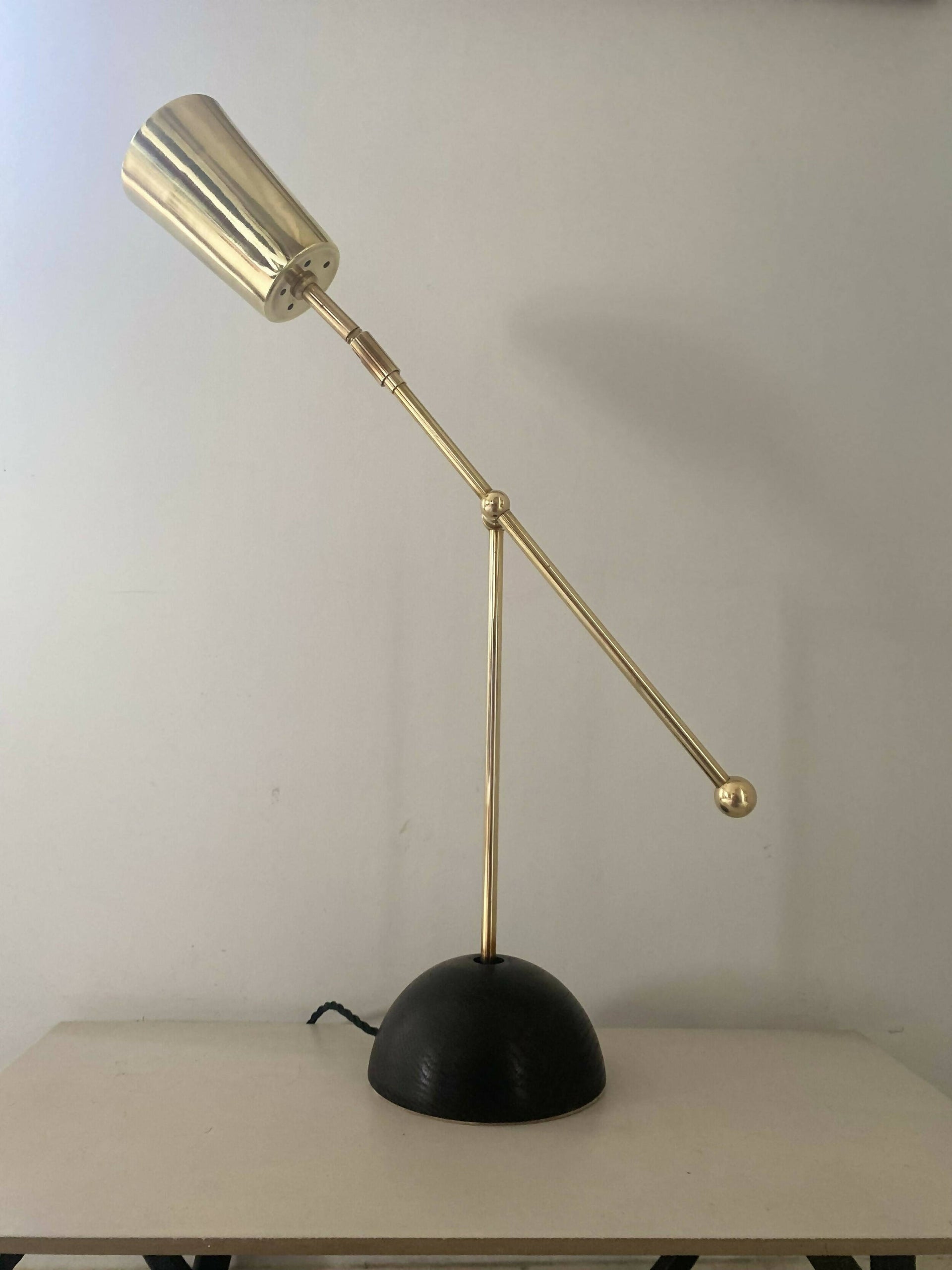 An elegant brass desk lamp with a hand turned solid oak base and a hand polished brass finish, positioned against a neutral background,  available  to buy on the-salon.com. SALON curates the finest , unique, handmade pieces from the interior industry's best makers and brands. Shop luxury furniture, lighting, rugs, art, antiques and vintage pieces and accessories from SALON interior designed rooms.