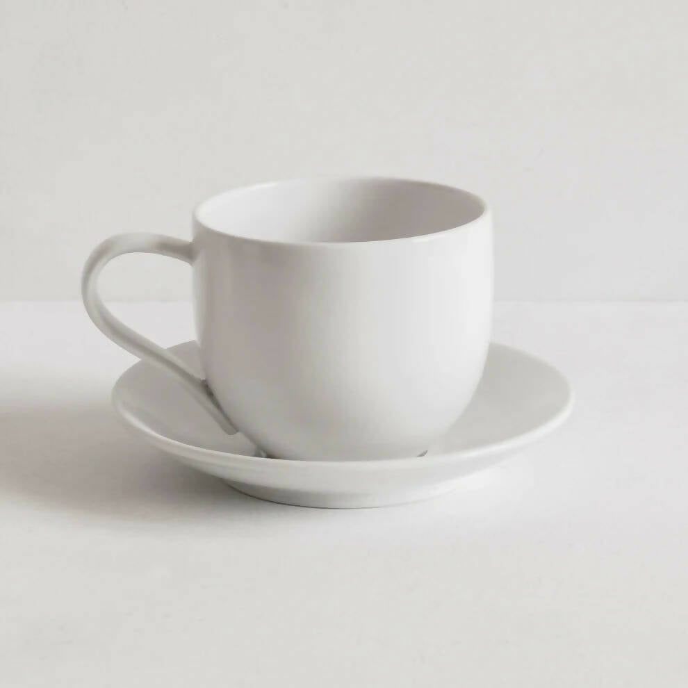 A white porcelain saucer designed to fit a mug, with a simple, clean design,  available  to buy on the-salon.com. SALON curates the finest , unique, handmade pieces from the interior industry's best makers and brands. Shop luxury furniture, lighting, rugs, art, antiques and vintage pieces and accessories from SALON interior designed rooms.