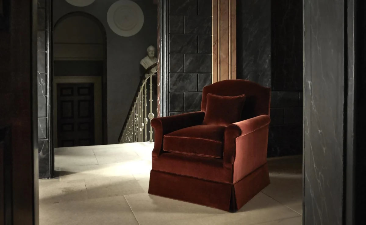 An elegant red upholstered armchair with a plush backrest and seat cushion, positioned in a stately home setting,  available  to buy on the-salon.com. SALON curates the finest , unique, handmade pieces from the interior industry's best makers and brands. Shop luxury furniture, lighting, rugs, art, antiques and vintage pieces and accessories from SALON interior designed rooms.