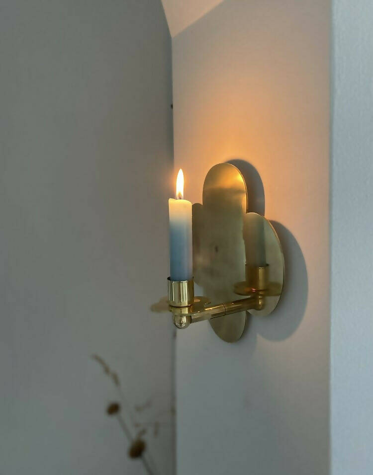 A solid brass wall-mounted candle sconce in the shape of a quatrefoil with  a candle,   available  to buy on the-salon.com. SALON curates the finest , unique, handmade pieces from the interior industry's best makers and brands. Shop luxury furniture, lighting, rugs, art, antiques and vintage pieces and accessories from SALON interior designed rooms.