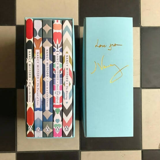 A set of five books with colorful spines in a blue box, with 'Love from Nancy' written in gold on the box's top and back,  available  to buy on the-salon.com. SALON curates the finest , unique, handmade pieces from the interior industry's best makers and brands. Shop luxury furniture, lighting, rugs, art, antiques and vintage pieces and accessories from SALON interior designed rooms.
