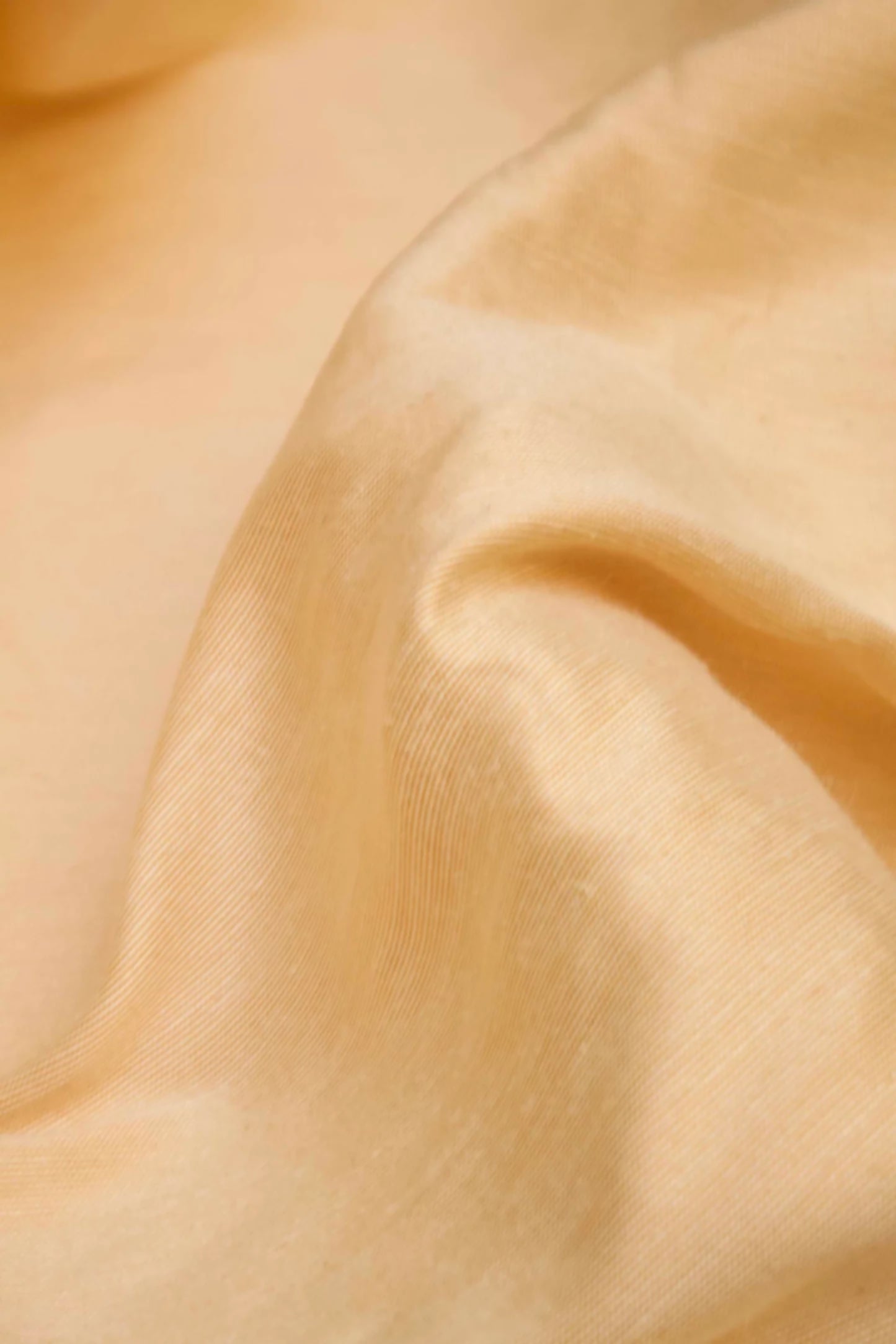 Close-up of a silk sateen fabric in a pale honey colour, showing its texture and sheen,  available  to buy on the-salon.com. SALON curates the finest , unique, handmade pieces from the interior industry's best makers and brands. Shop luxury furniture, lighting, rugs, art, antiques and vintage pieces and accessories from SALON interior designed rooms.