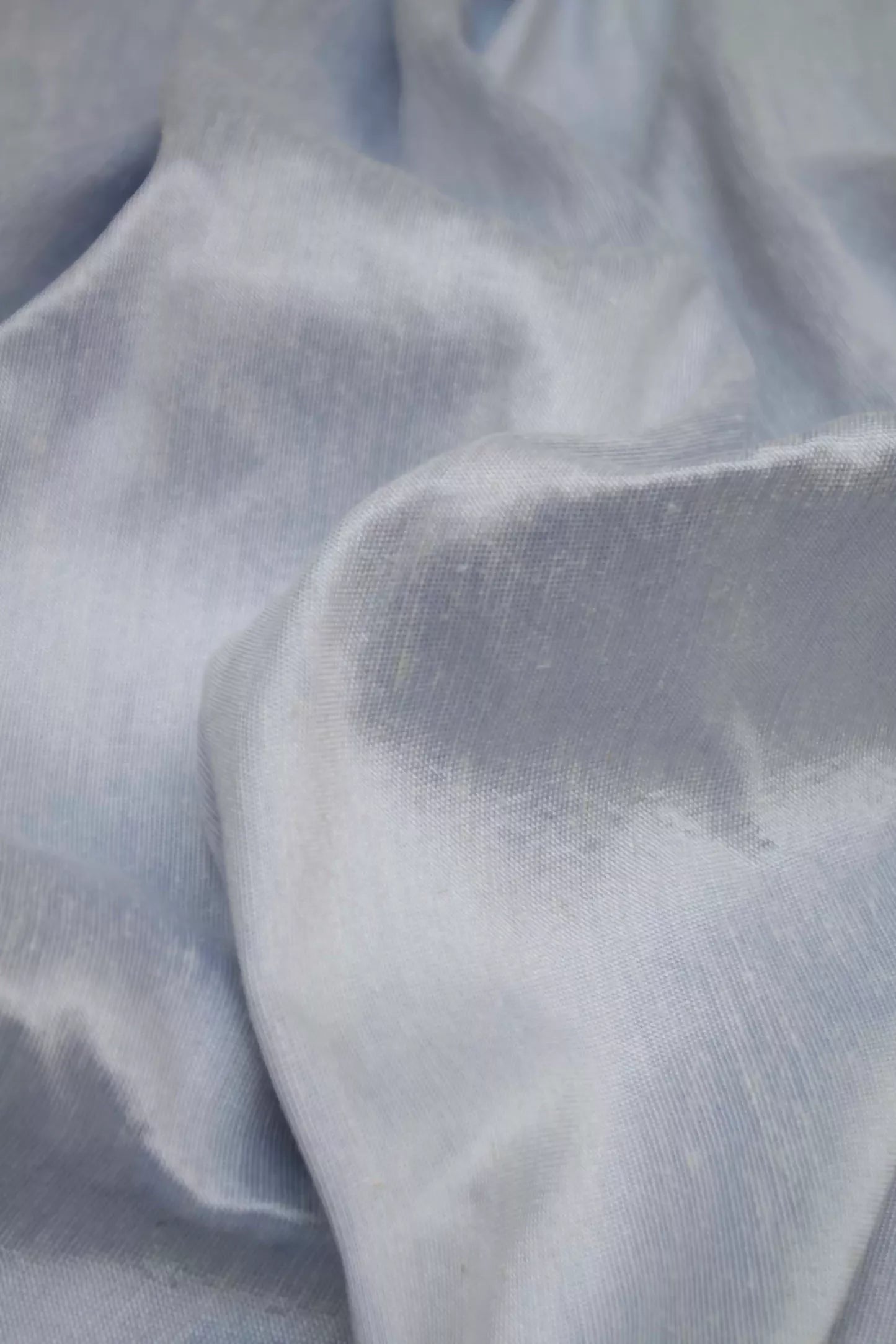 A close-up image of silk sateen fabric in a sky blue colour, displaying its texture and sheen,  available  to buy on the-salon.com. SALON curates the finest , unique, handmade pieces from the interior industry's best makers and brands. Shop luxury furniture, lighting, rugs, art, antiques and vintage pieces and accessories from SALON interior designed rooms.