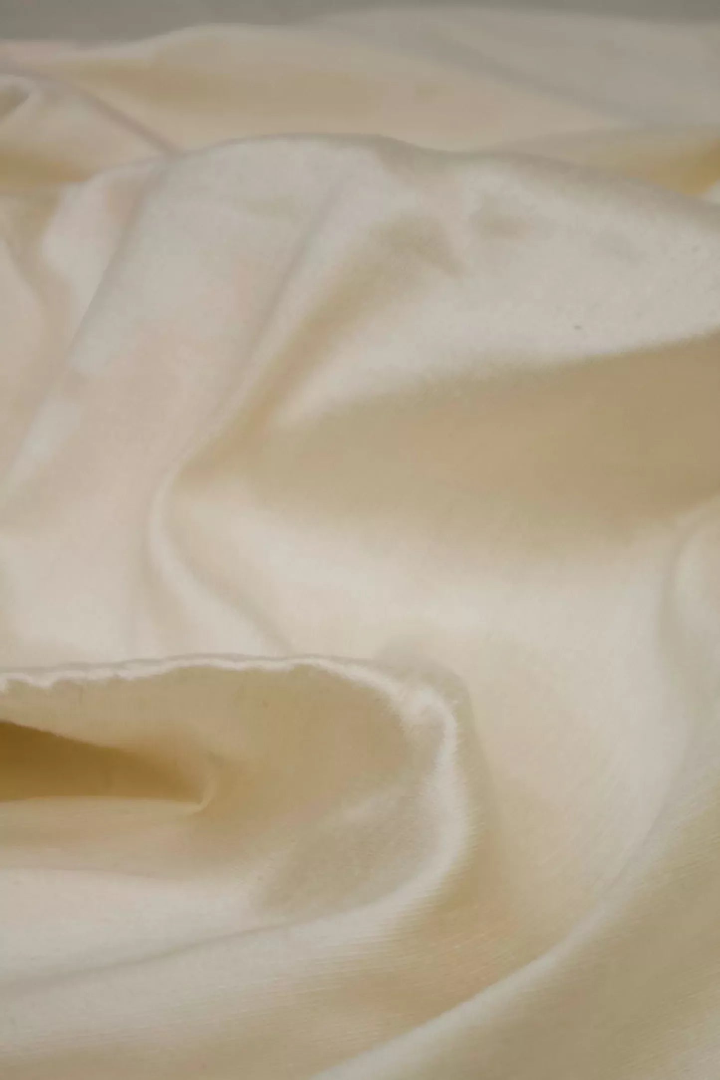 Close-up of a silk sateen fabric in a champagne colour, displaying its texture and sheen,  available  to buy on the-salon.com. SALON curates the finest , unique, handmade pieces from the interior industry's best makers and brands. Shop luxury furniture, lighting, rugs, art, antiques and vintage pieces and accessories from SALON interior designed rooms.