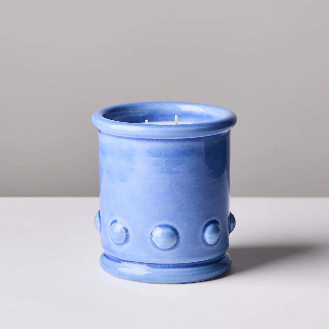 Blue ceramic candle vessel with spherical detailing on the sides, with a candle visible at the top. The vessel is placed against a neutral background,  available  to buy on the-salon.com. SALON curates the finest , unique, handmade pieces from the interior industry's best makers and brands. Shop luxury furniture, lighting, rugs, art, antiques and vintage pieces and accessories from SALON interior designed rooms.