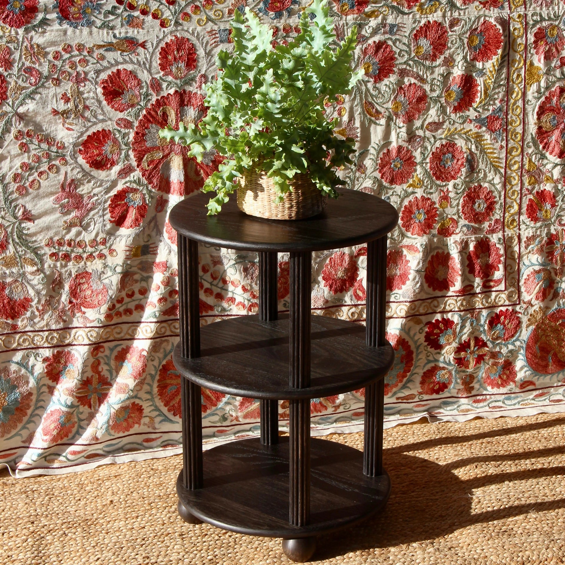 Dark wooden side table with a plant against a colorful floral backdrop,  available  to buy on the-salon.com. SALON curates the finest , unique, handmade pieces from the interior industry's best makers and brands. Shop luxury furniture, lighting, rugs, art, antiques and vintage pieces and accessories from SALON interior designed rooms.