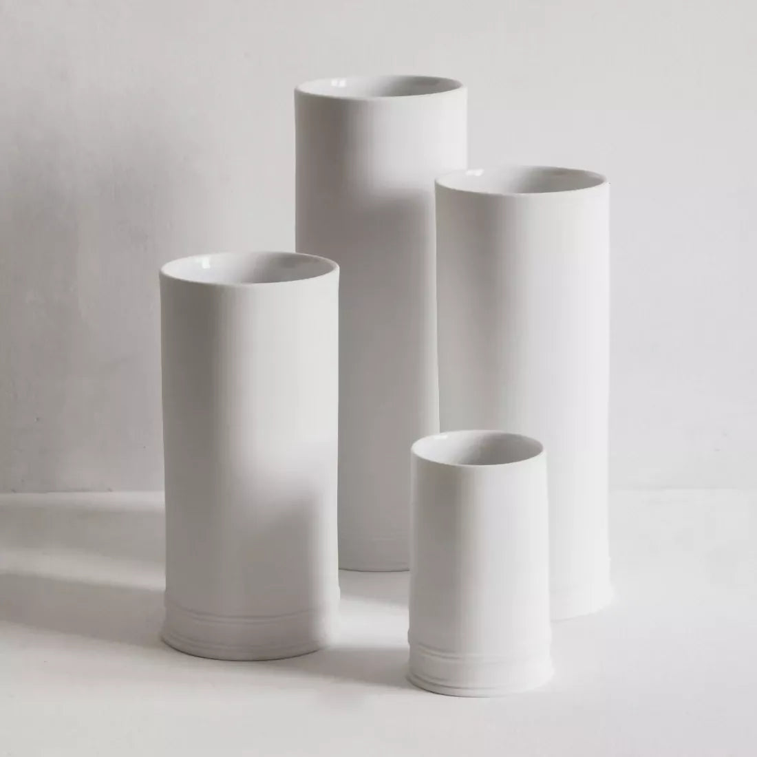 A white, cylindrical, porcelain column vase with an unglazed exterior, displayed against a neutral background,  available  to buy on the-salon.com. SALON curates the finest , unique, handmade pieces from the interior industry's best makers and brands. Shop luxury furniture, lighting, rugs, art, antiques and vintage pieces and accessories from SALON interior designed rooms.