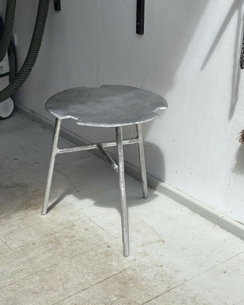 Small metal stool in a room with a vacuum cleaner and broom in the background.