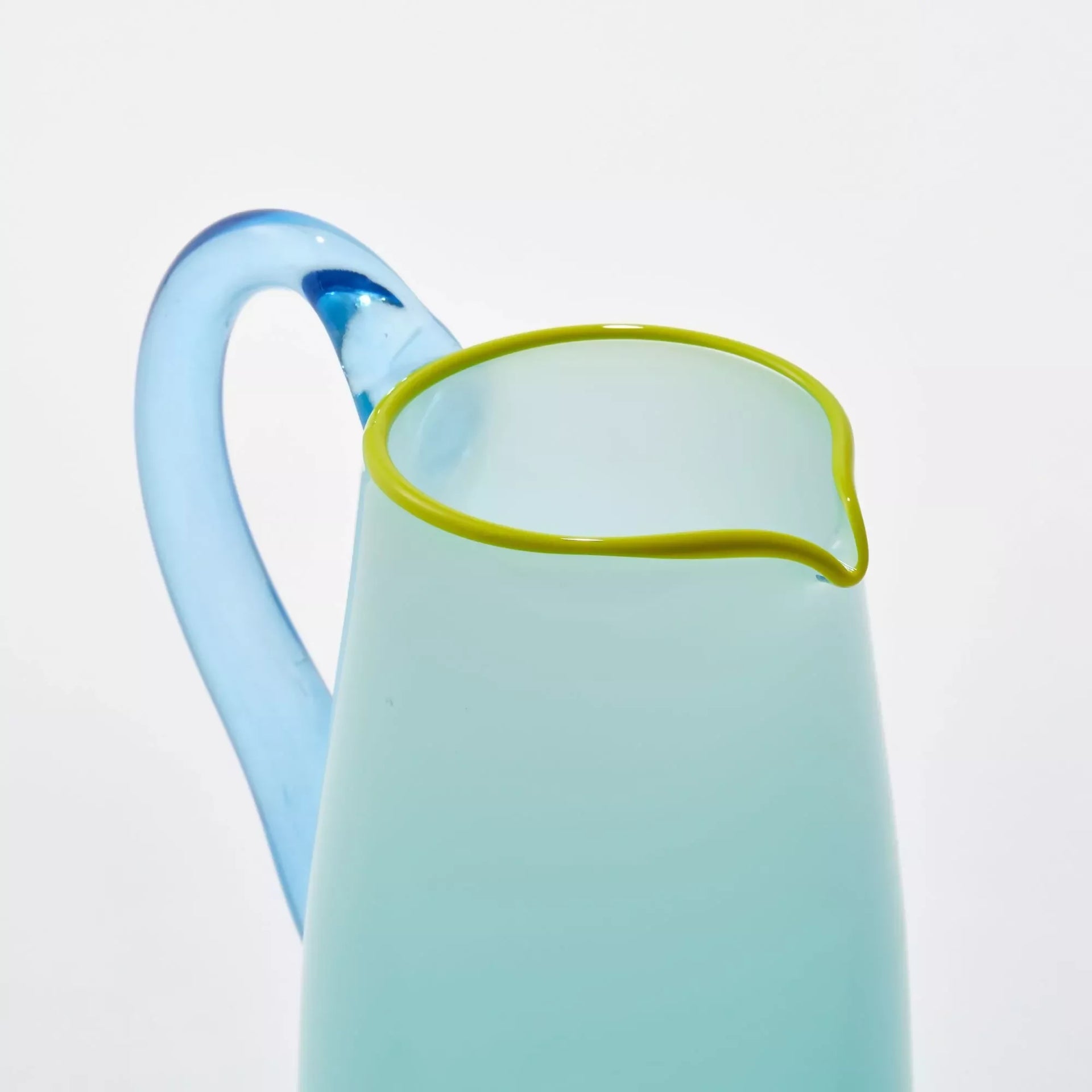 An image of the hand-blown blue glass milk jug with an aqua blue handle and a celadon lip, against a white background- available  to buy on the-salon.com. SALON curates the finest , unique, handmade pieces from the interior industry's best makers and brands. Shop luxury furniture, lighting, rugs, art, antiques and vintage pieces and accessories from SALON interior designed rooms.
