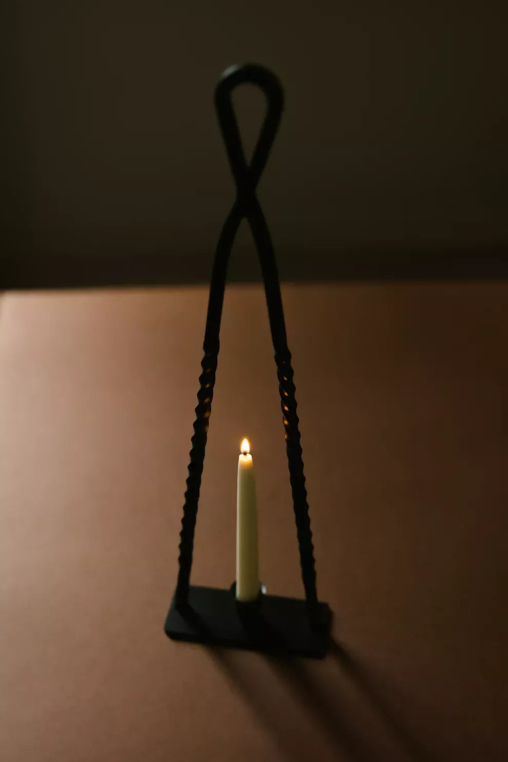 A black, handmade steel Alchemy candle holder by HUEY, displayed on a brown background with a candle inside it, available  to buy on the-salon.com. SALON curates the finest , unique, handmade pieces from the interior industry's best makers and brands. Shop luxury furniture, lighting, rugs, art, antiques and vintage pieces and accessories from SALON interior designed rooms.
