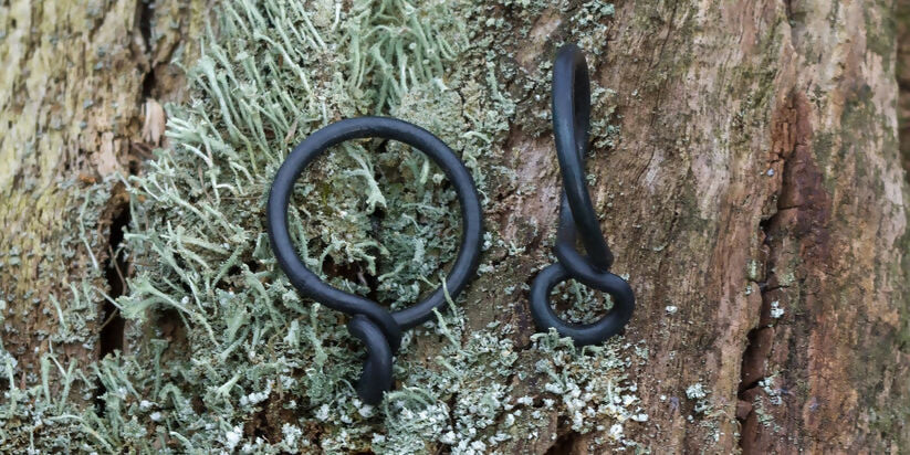A black wrought iron curtain ring hanging on a wooden surface, with a natural outdoor background,  available  to buy on the-salon.com. SALON curates the finest , unique, handmade pieces from the interior industry's best makers and brands. Shop luxury furniture, lighting, rugs, art, antiques and vintage pieces and accessories from SALON interior designed rooms.