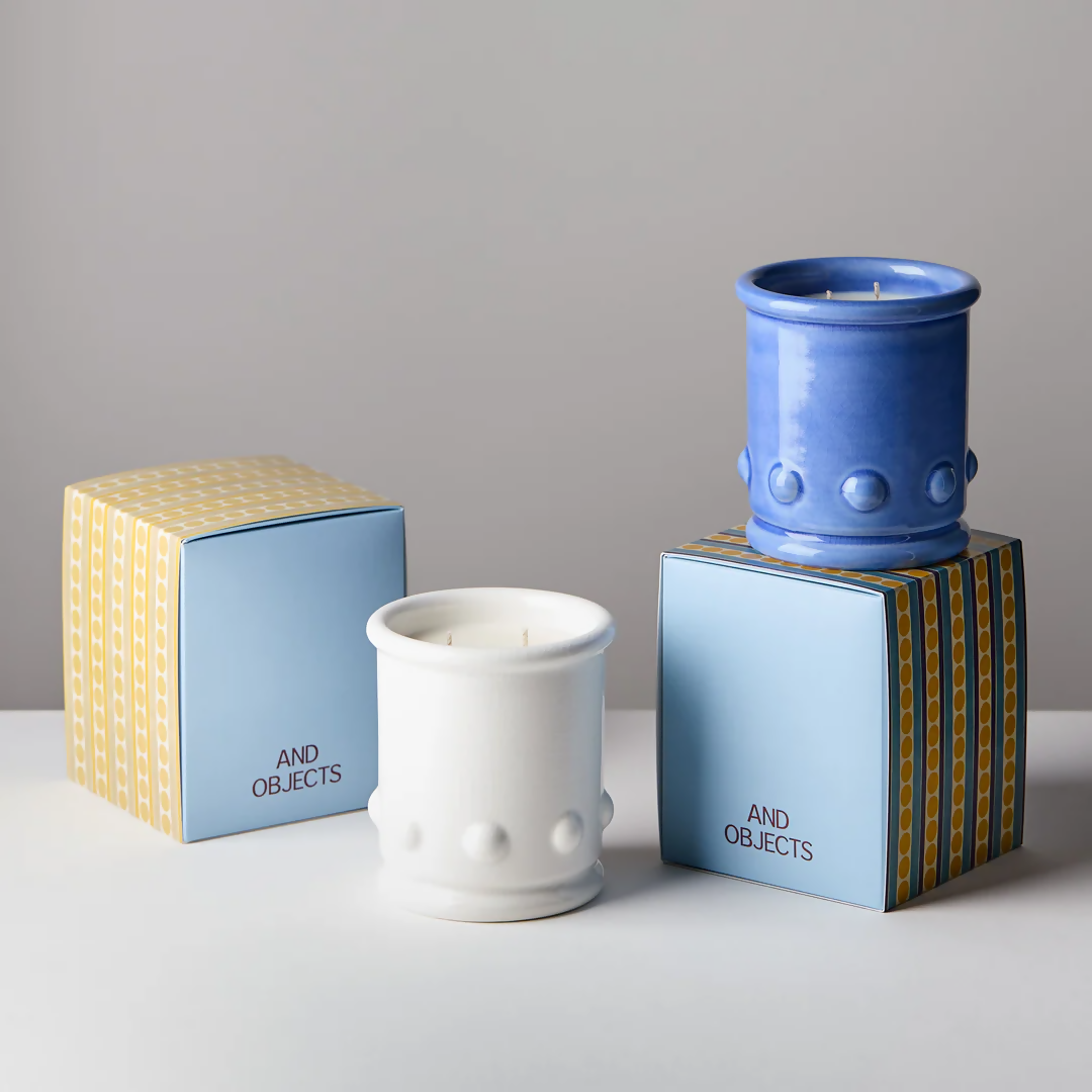 Blue and white ceramic candle vessels with spherical detailing on the sides, with a candle visible at the top. The vessel is placed against a neutral background,  available  to buy on the-salon.com. SALON curates the finest , unique, handmade pieces from the interior industry's best makers and brands. Shop luxury furniture, lighting, rugs, art, antiques and vintage pieces and accessories from SALON interior designed rooms.