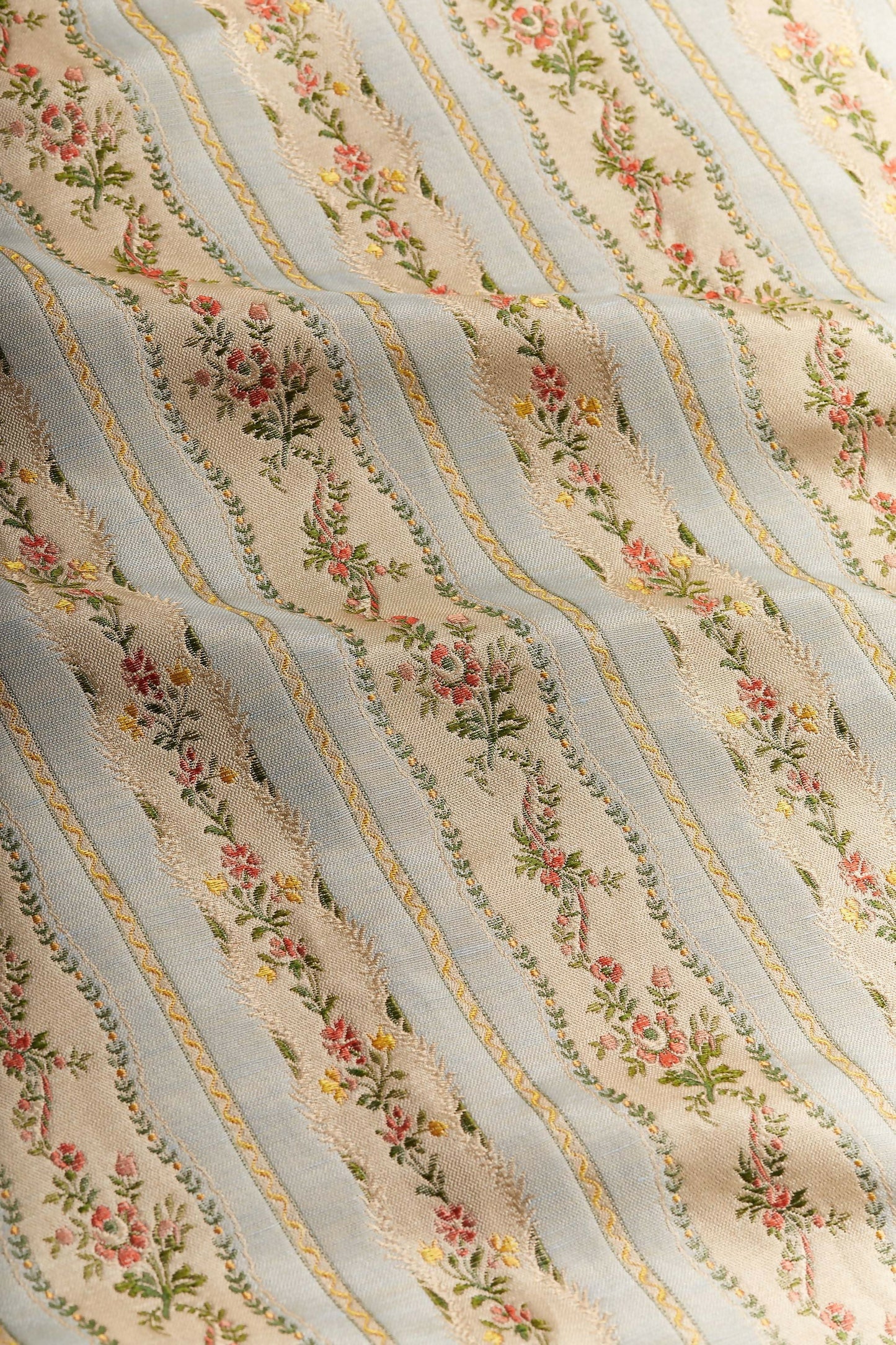 Close-up of Spitalfields stripe sky fabric featuring a jacquard weave with floral motifs and silk leaves, in a warm honey tone,  available  to buy on the-salon.com. SALON curates the finest , unique, handmade pieces from the interior industry's best makers and brands. Shop luxury furniture, lighting, rugs, art, antiques and vintage pieces and accessories from SALON interior designed rooms.
