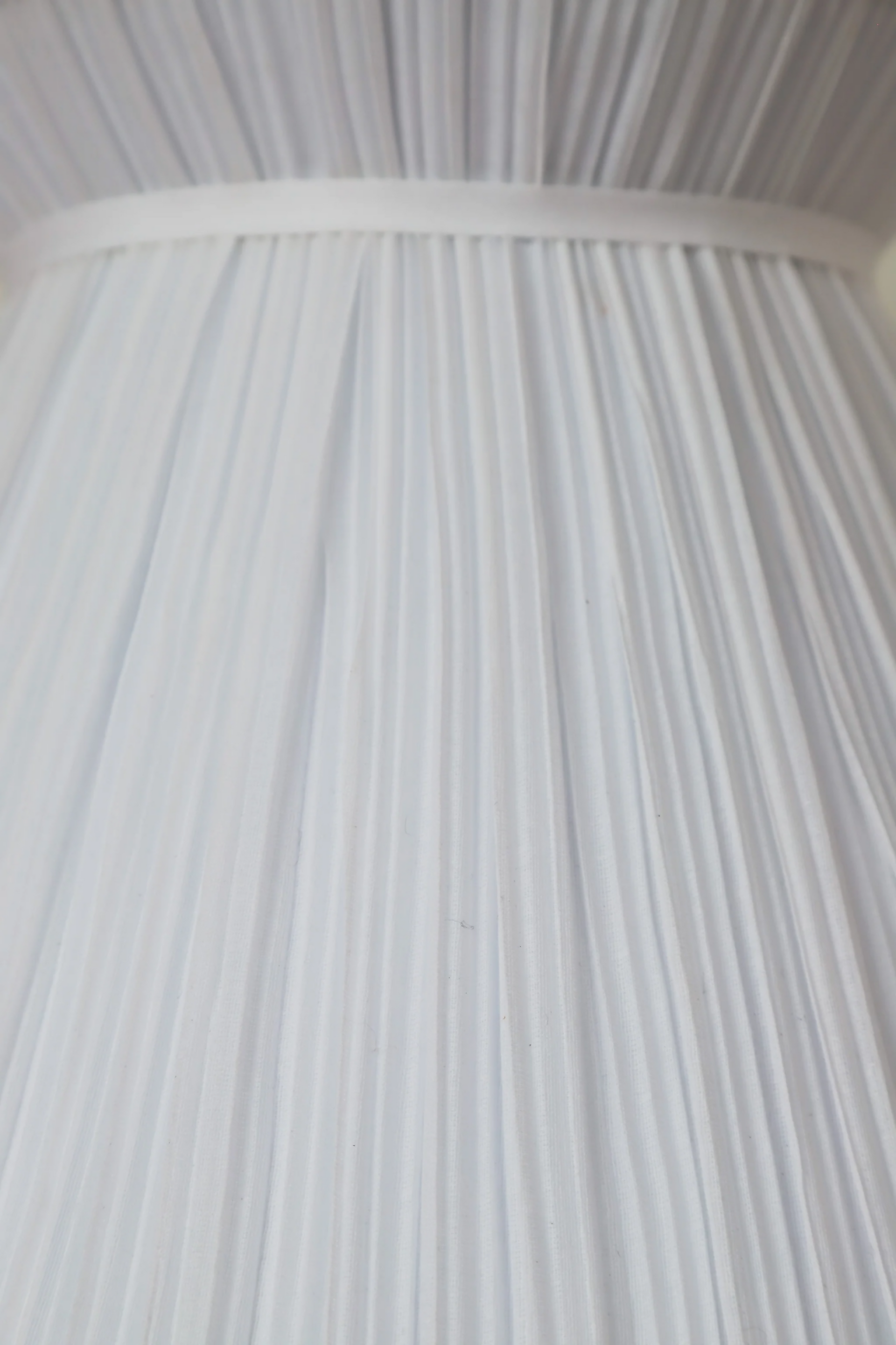 A white pleated pendant light hanging in a room with decorative walls, displaying a soft illumination, available  to buy on the-salon.com. SALON curates the finest , unique, handmade pieces from the interior industry's best makers and brands. Shop luxury furniture, lighting, rugs, art, antiques and vintage pieces and accessories from SALON interior designed rooms.