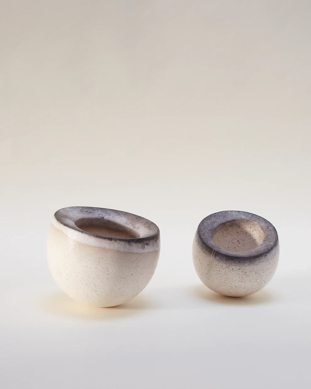 A pair of beige ceramic bowls with a textured surface, one with an open top view and the other with a side view showing the interior,  available  to buy on the-salon.com. SALON curates the finest , unique, handmade pieces from the interior industry's best makers and brands. Shop luxury furniture, lighting, rugs, art, antiques and vintage pieces and accessories from SALON interior designed rooms.