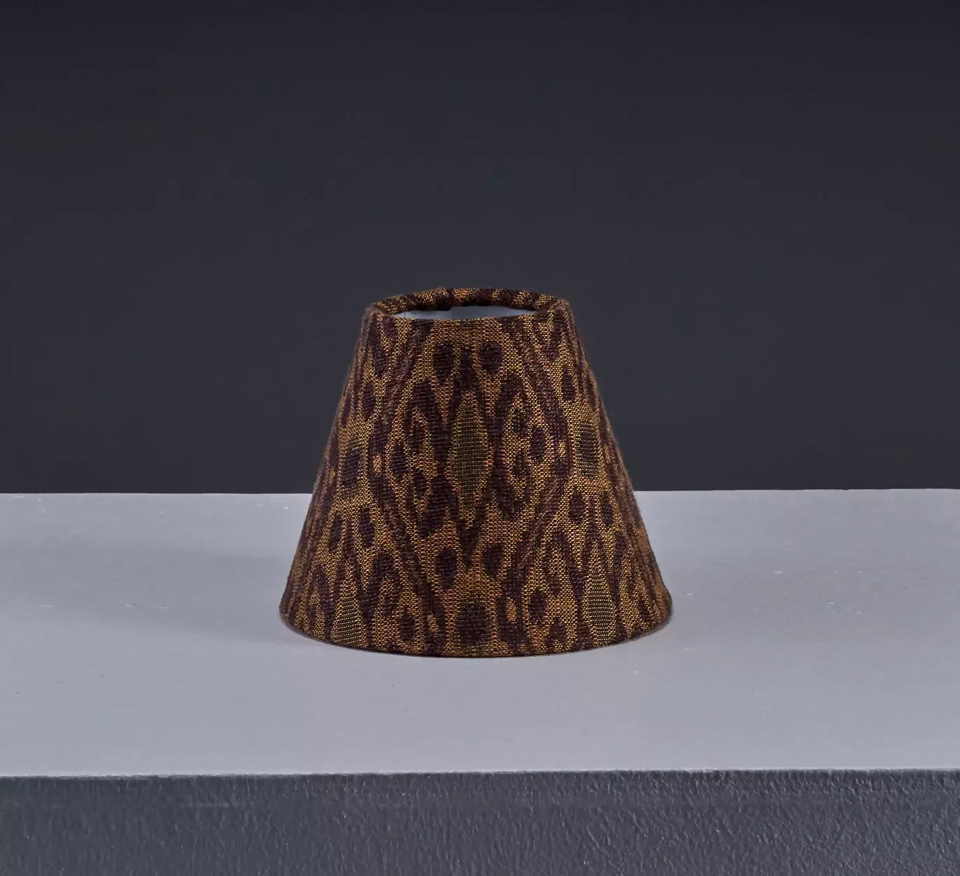 A lampshade with a woven ikat pattern, featuring a geometric design in a tiger's eye color, against a white background,  available  to buy on the-salon.com. SALON curates the finest , unique, handmade pieces from the interior industry's best makers and brands. Shop luxury furniture, lighting, rugs, art, antiques and vintage pieces and accessories from SALON interior designed rooms.