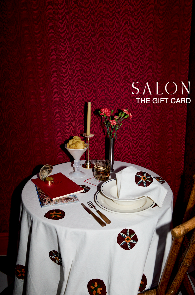 Dining table setting with a red wall and 'Salon' branding.
