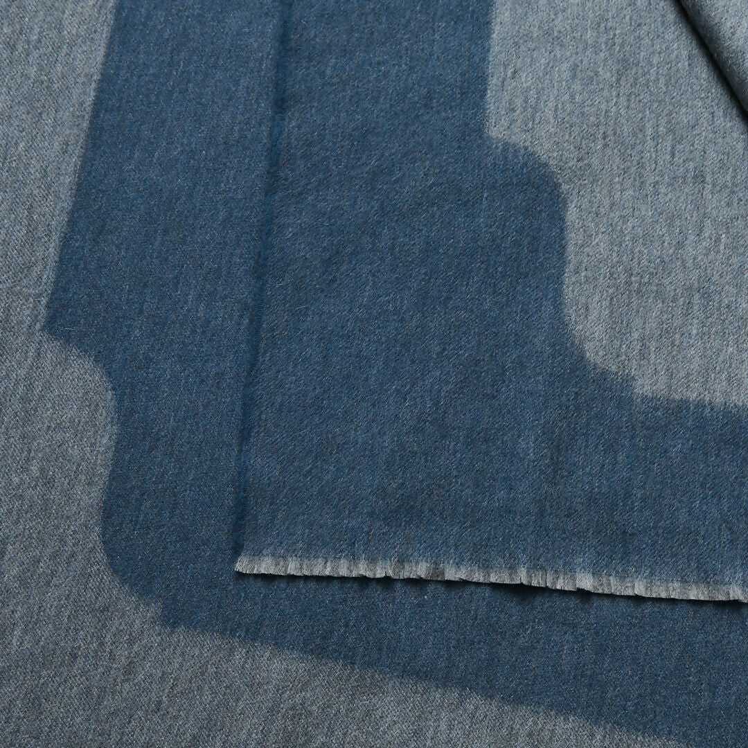 A folded slate blue cashmere throw blanket with a decorative border detail,  available  to buy on the-salon.com. SALON curates the finest , unique, handmade pieces from the interior industry's best makers and brands. Shop luxury furniture, lighting, rugs, art, antiques and vintage pieces and accessories from SALON interior designed rooms.
