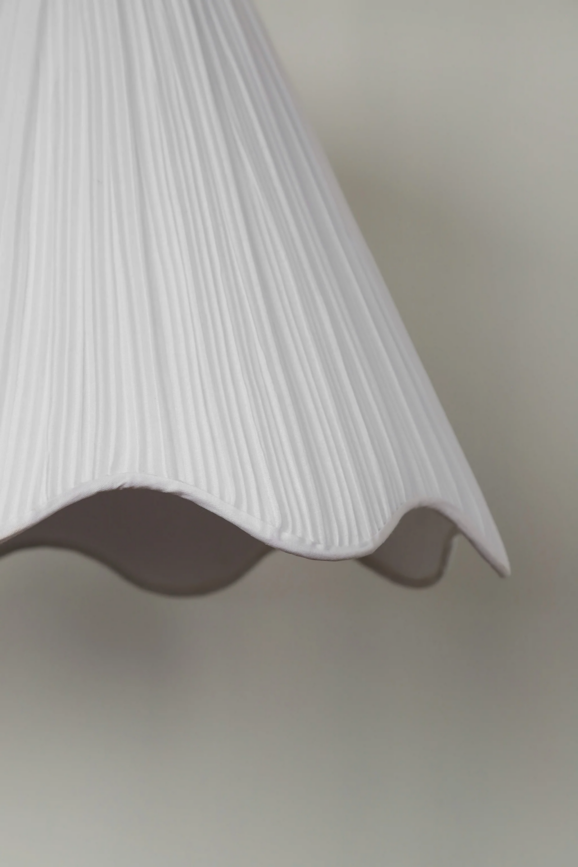 A white pleated pendant light hanging in a room with decorative walls, displaying a soft illumination, available  to buy on the-salon.com. SALON curates the finest , unique, handmade pieces from the interior industry's best makers and brands. Shop luxury furniture, lighting, rugs, art, antiques and vintage pieces and accessories from SALON interior designed rooms.