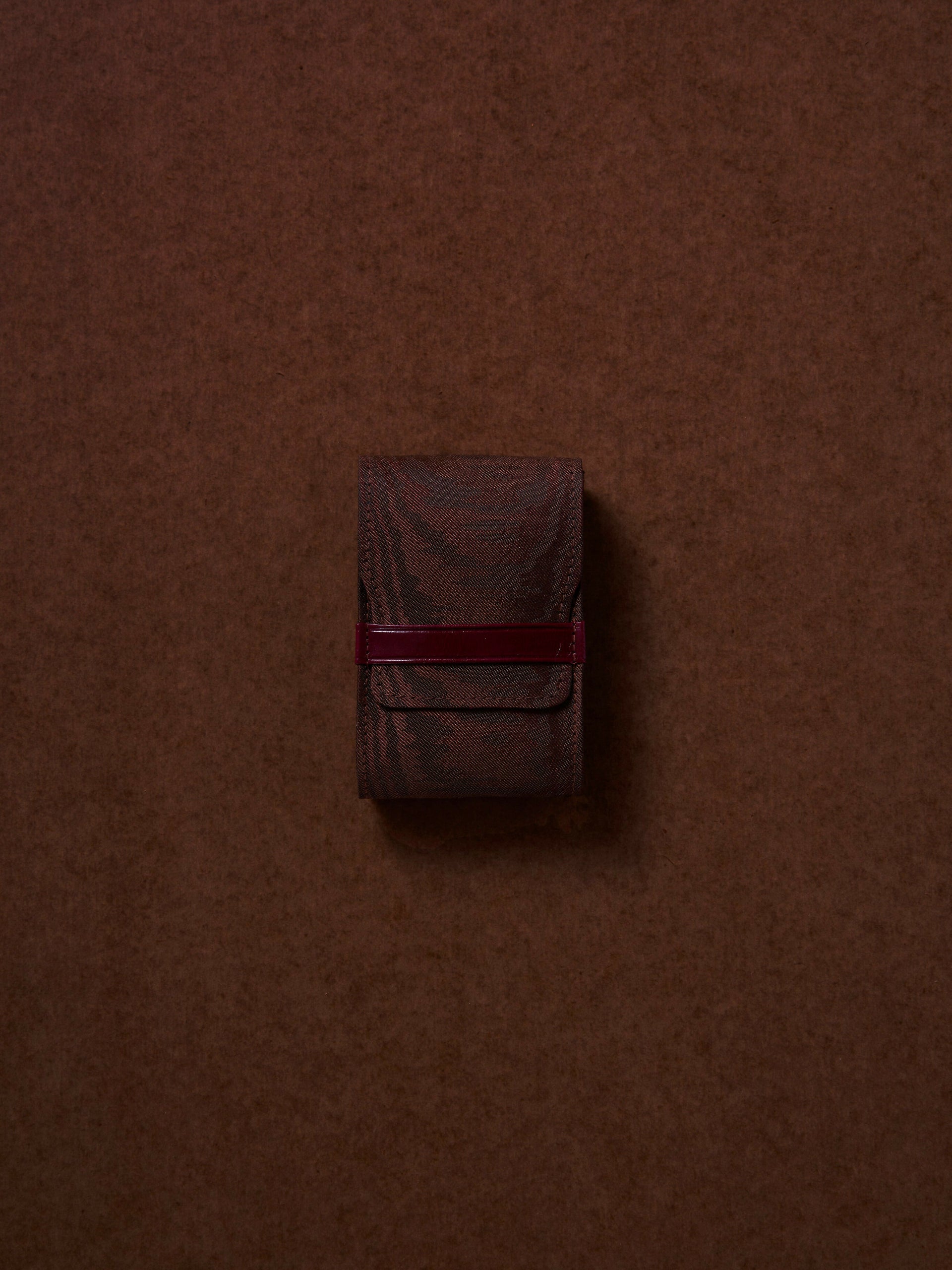 Small brown leather pouch with a red strap on a brown background,  available  to buy on the-salon.com. SALON curates the finest , unique, handmade pieces from the interior industry's best makers and brands. Shop luxury furniture, lighting, rugs, art, antiques and vintage pieces and accessories from SALON interior designed rooms.